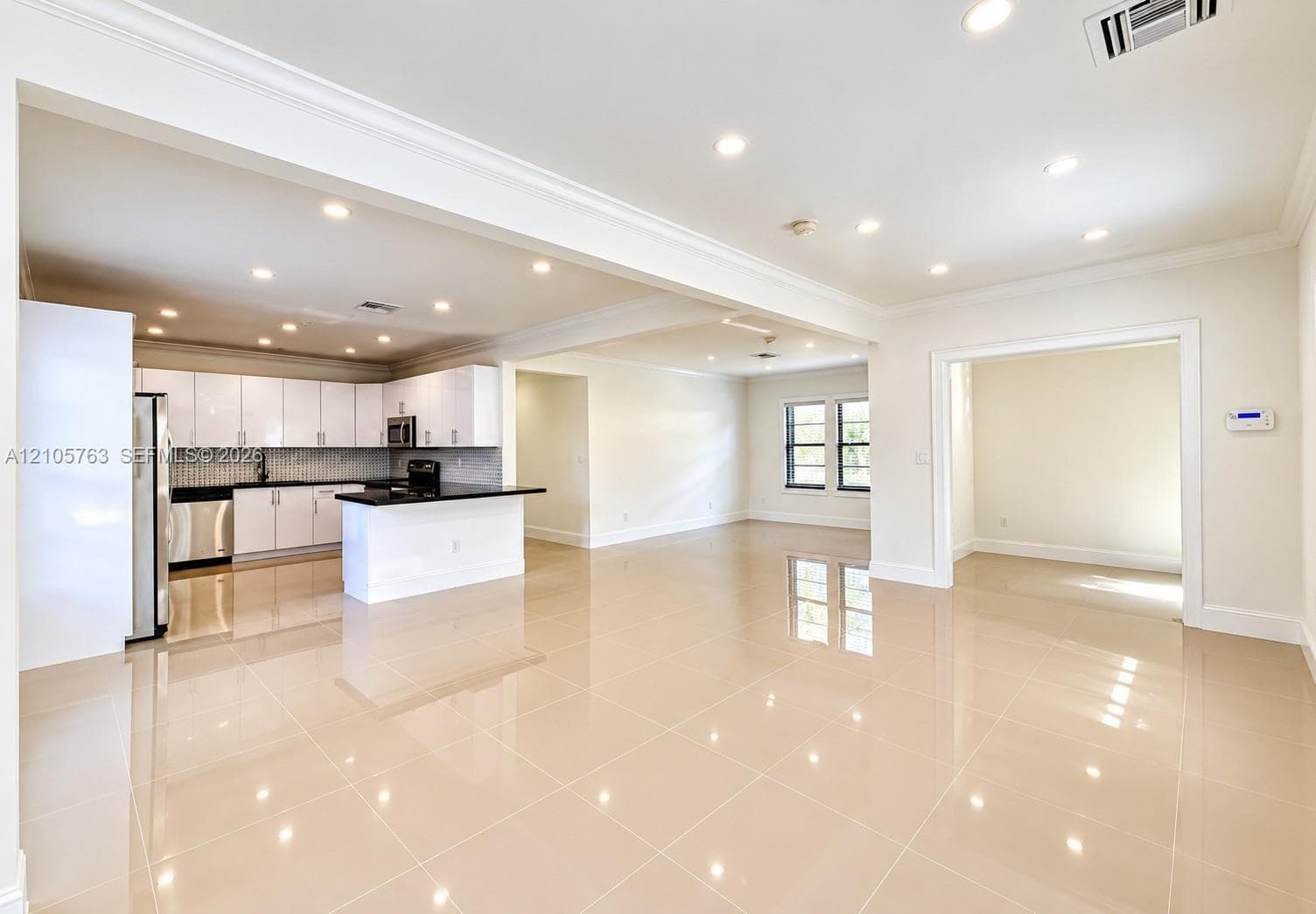 Open-concept interior featuring large-format tile flooring, recessed ceiling lighting, crown molding, a kitchen island with stone countertops, and crisp white cabinetry