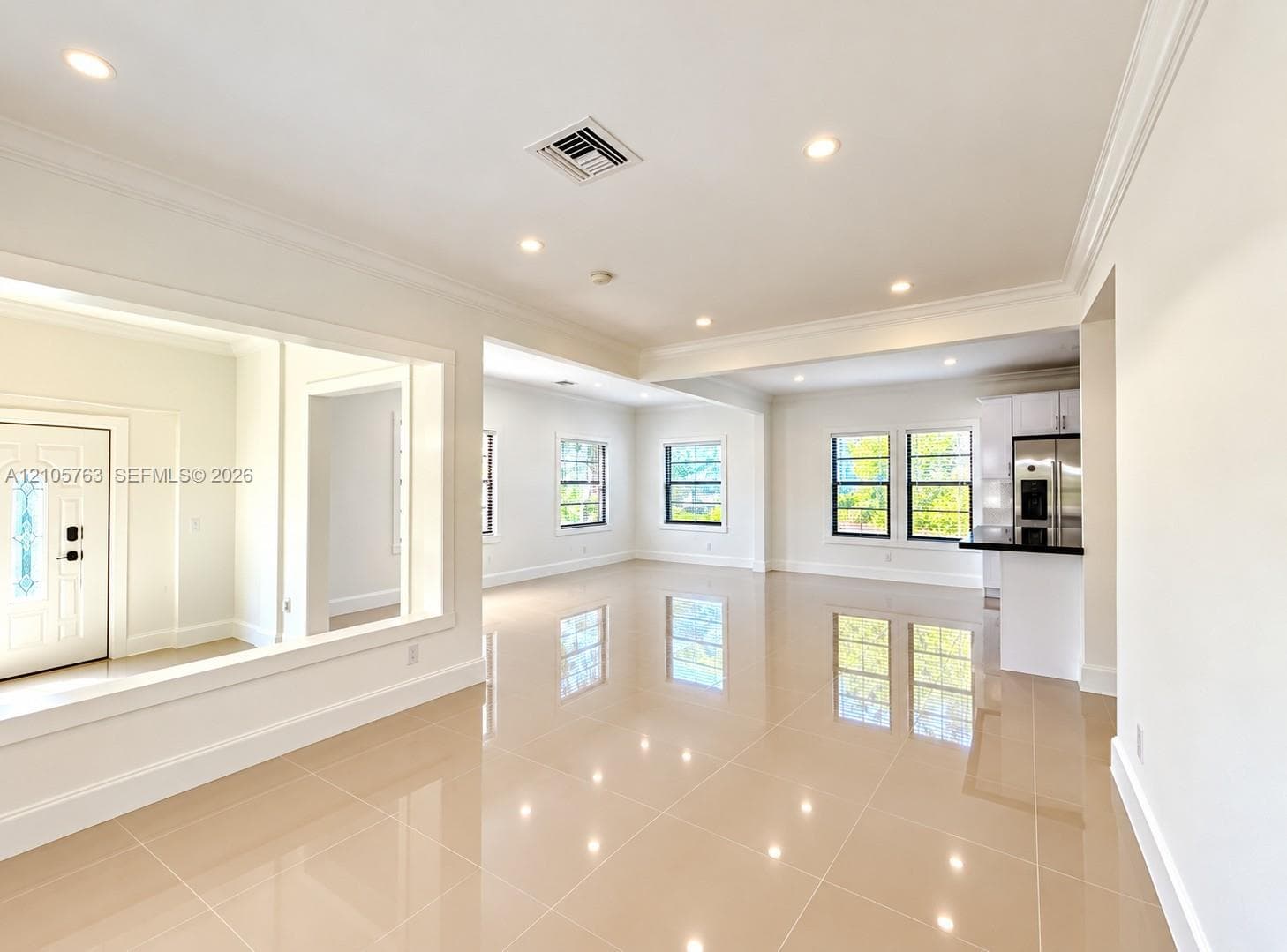 Open-concept living space featuring high-gloss tile flooring, crown molding, recessed lighting, and large windows with black frames