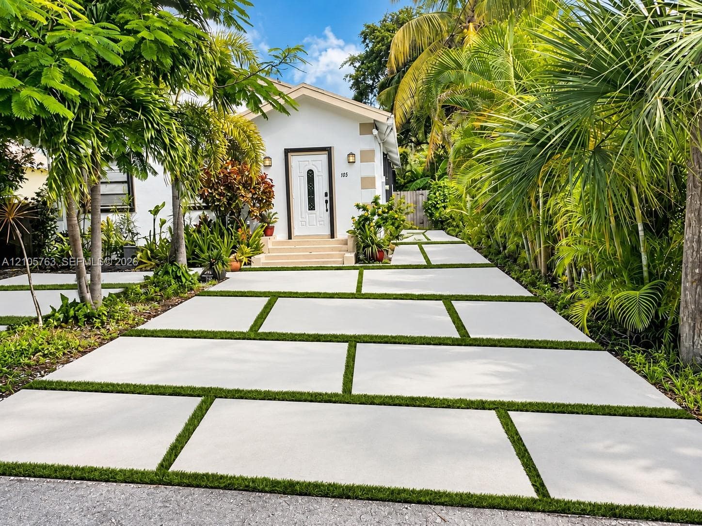 Exterior facade featuring white stucco walls, decorative quoins, a white paneled front door with glass inlay, and a concrete paver driveway with integrated turf strips