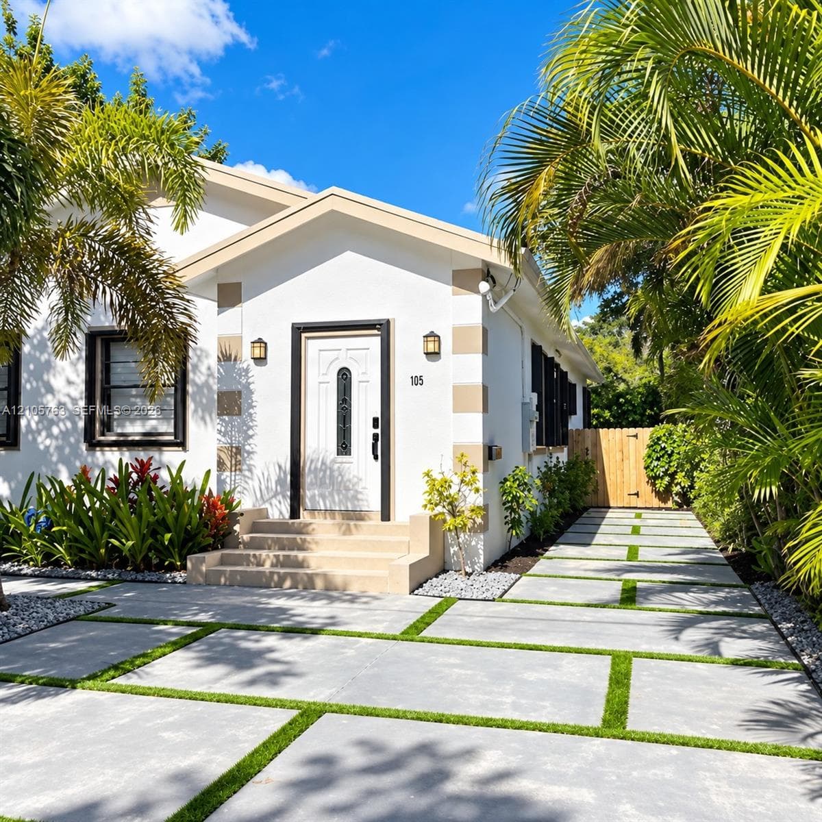 Exterior facade featuring white stucco finish with contrasting corner quoins, a concrete paver driveway with turf accents, a multi-paneled entry door with decorative glass insert, and tiered concrete steps