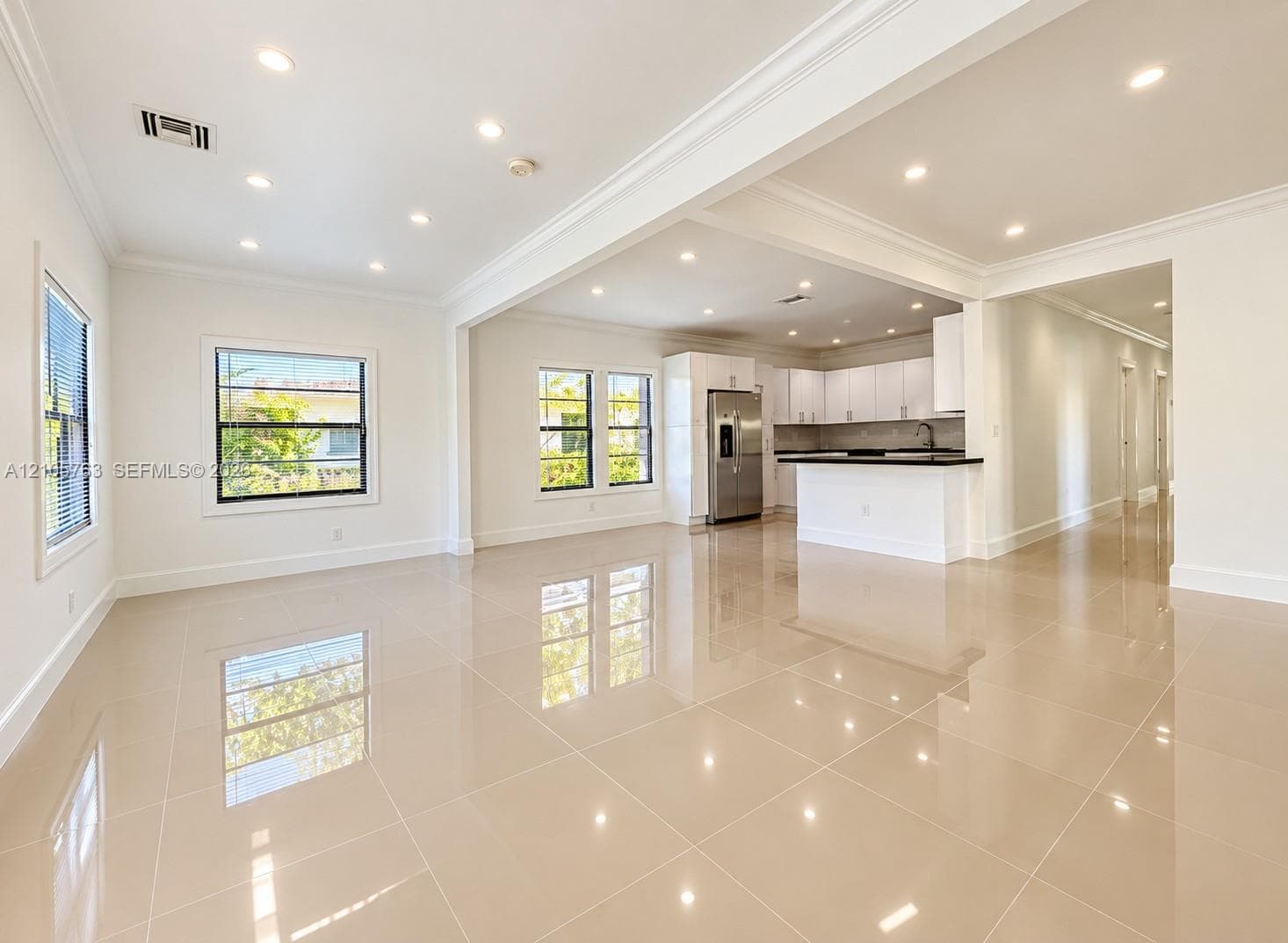 Large-format polished tile flooring, recessed ceiling lighting, crown molding, kitchen with white cabinetry, and a peninsula with a contrasting countertop
