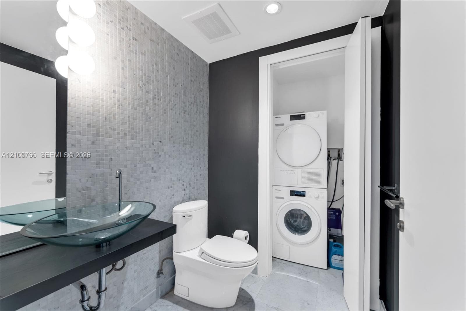 Half bath with glass vessel sink, mosaic tile and the stacked Miele washer and dryer.