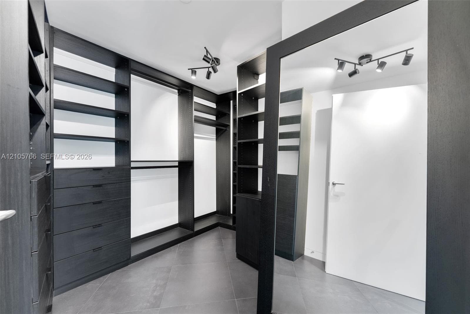 Primary walk-in closet with built-in drawers, shelving, hanging space and a floor mirror.