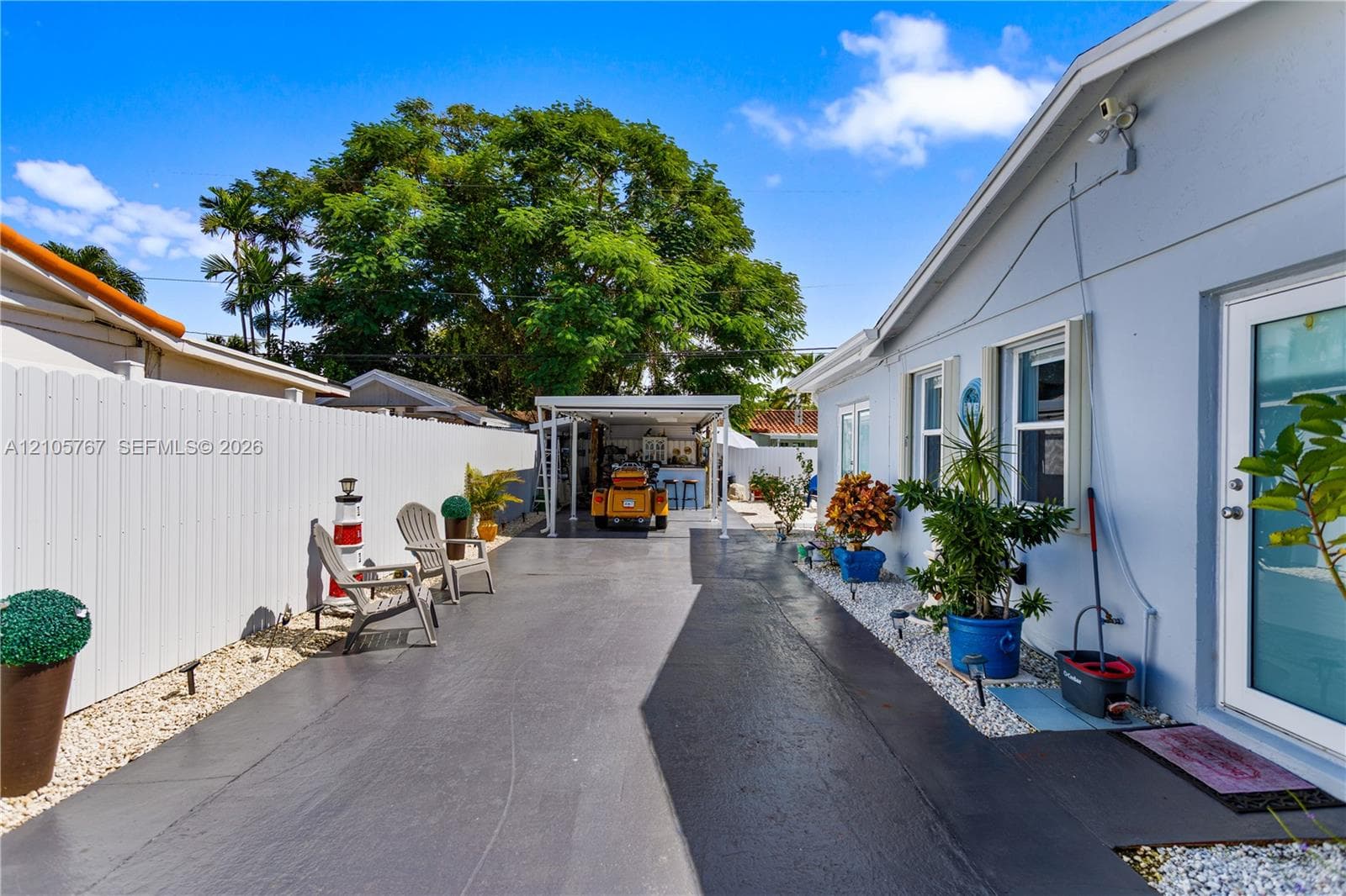 Paved driveway featuring a white vinyl privacy fence, stone landscaping, and a covered carport