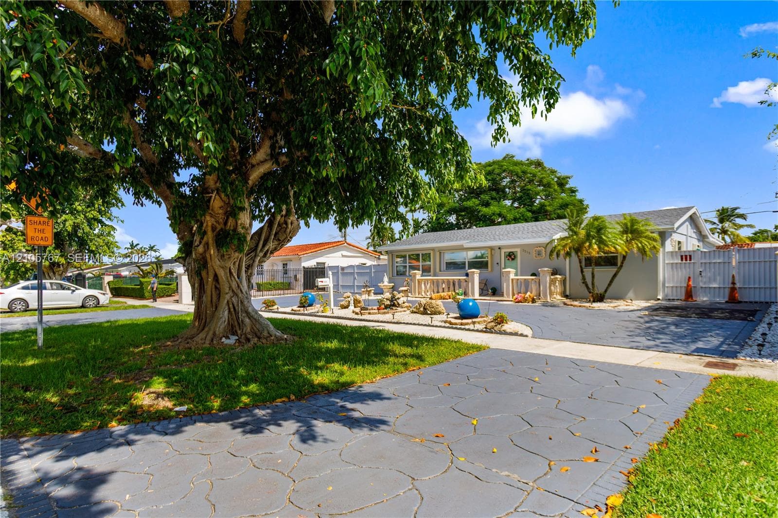 Single-story exterior featuring a stamped concrete driveway, decorative balustrade, mature landscaping, and a white privacy fence