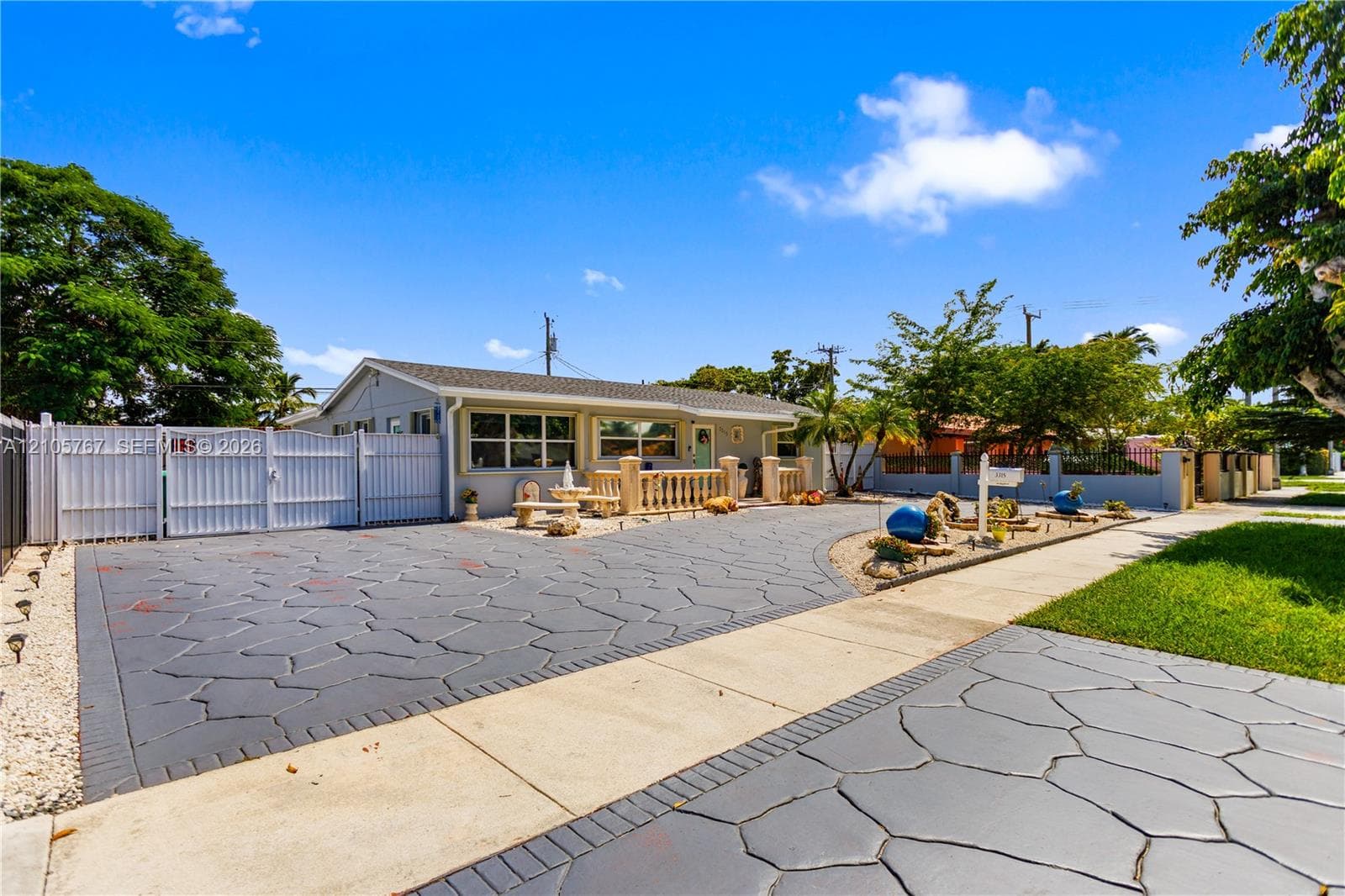 Single-story residence featuring a stamped concrete driveway, decorative stone balustrade, white vinyl perimeter fencing, and mature landscaping