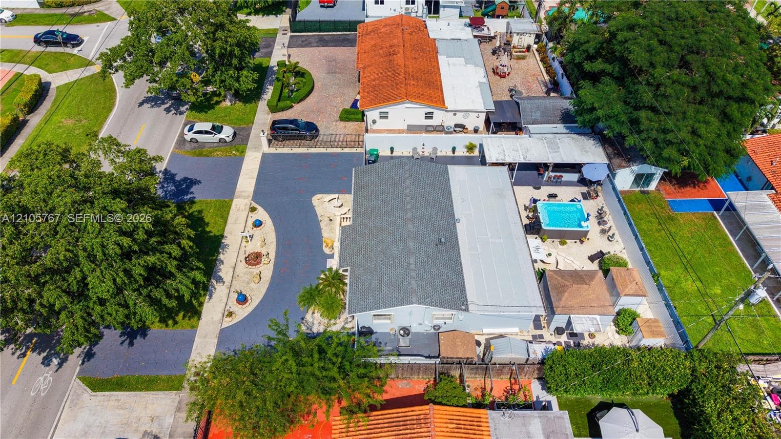 Aerial perspective of a property featuring an expansive asphalt driveway, a rectangular swimming pool, and dedicated hardscaped patio areas