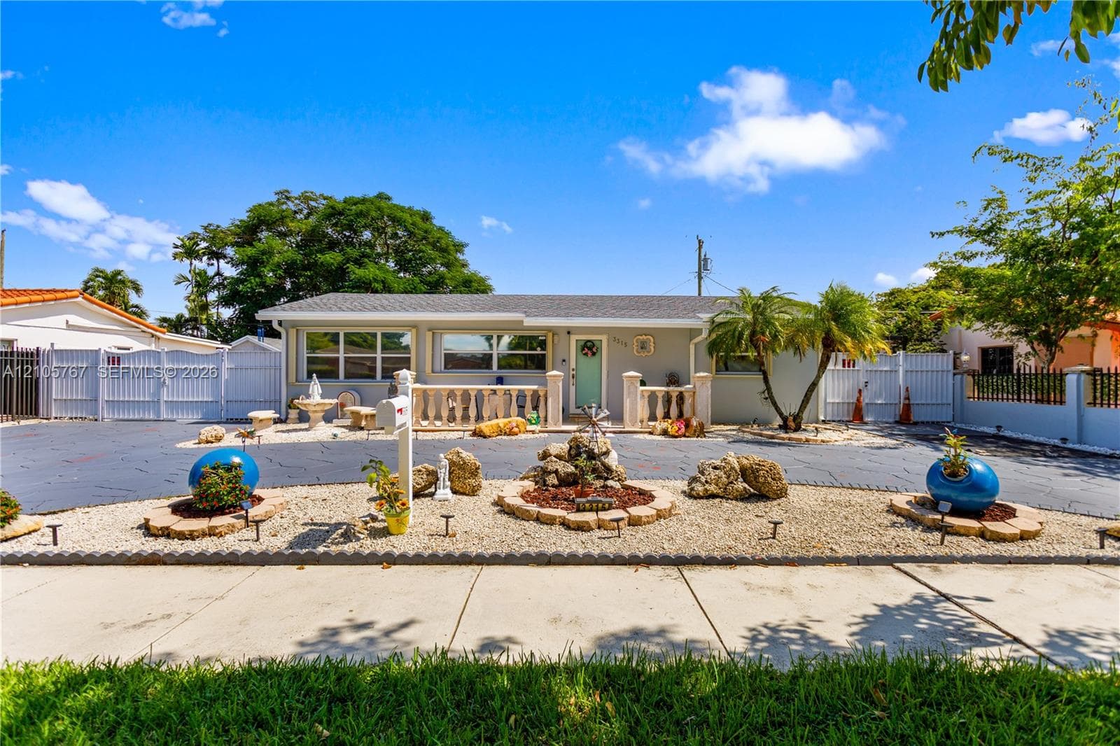 Single-story residence featuring a paved courtyard, decorative stone balustrade, rock garden landscaping, and white perimeter fencing