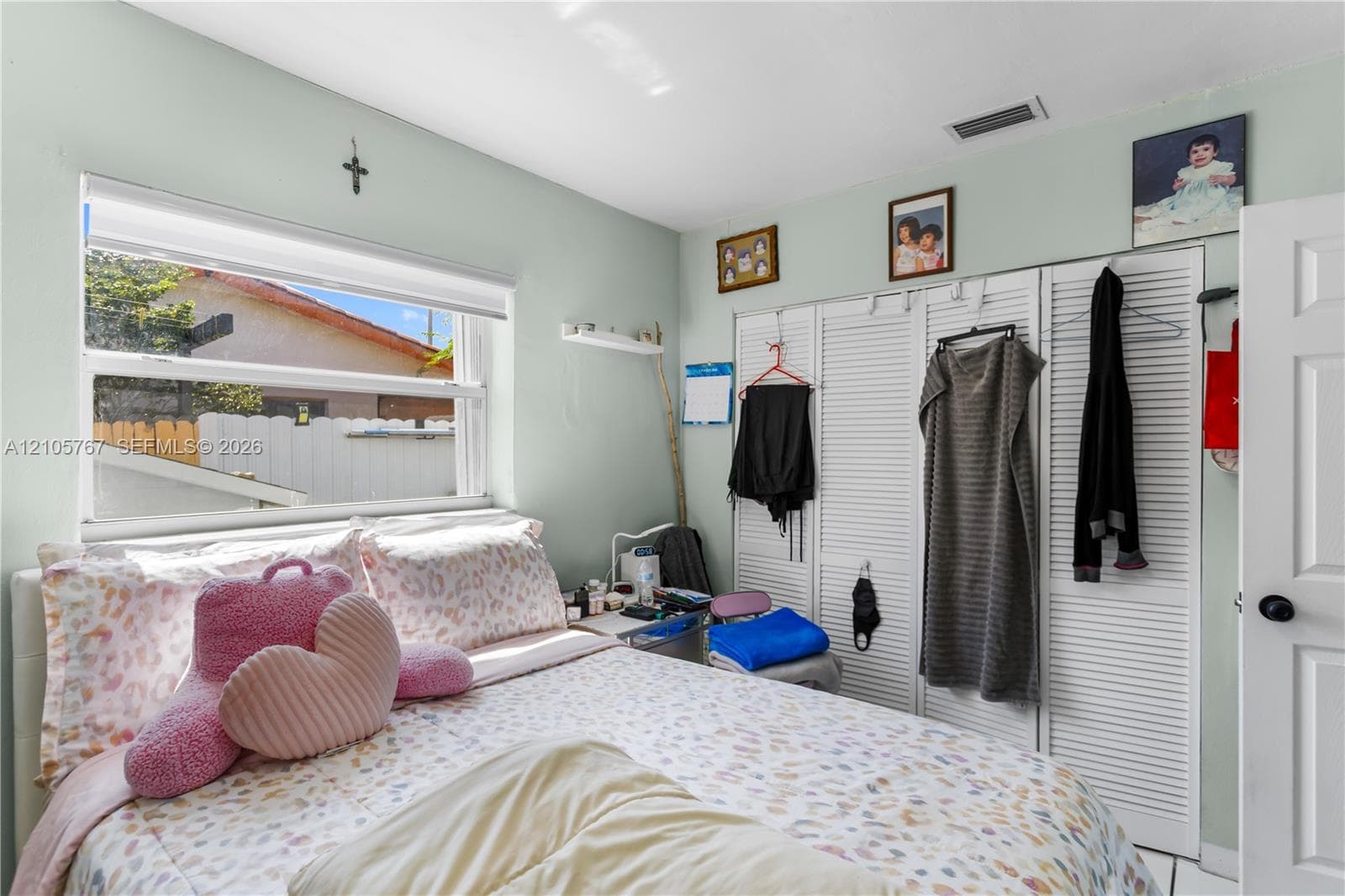 Room featuring a dual-pane window with a white roller shade and floor-to-ceiling white louvered closet doors