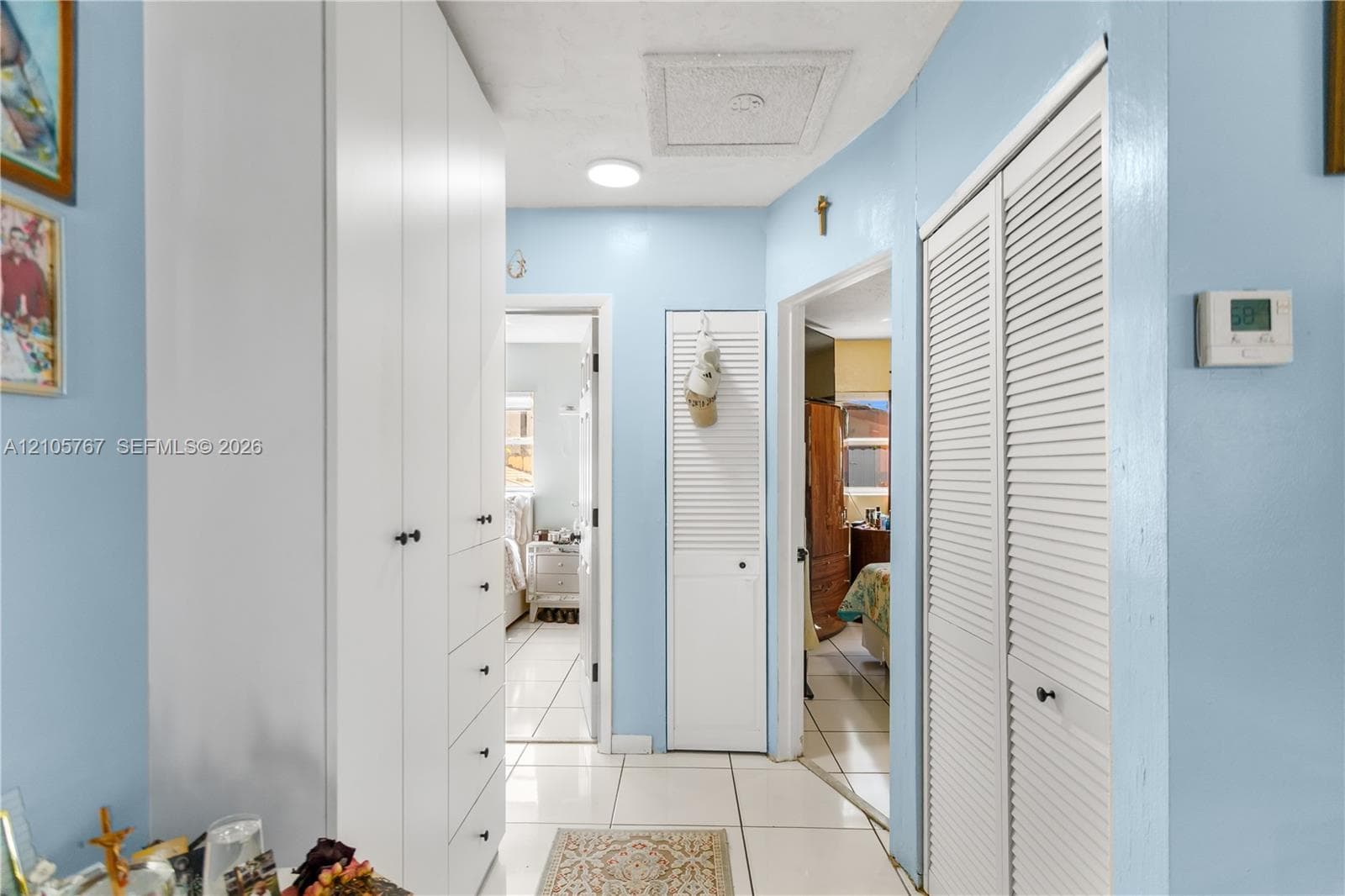 Hallway featuring floor-to-ceiling white cabinetry, integrated drawer storage, and white louvered closet doors throughout with high-gloss tile flooring