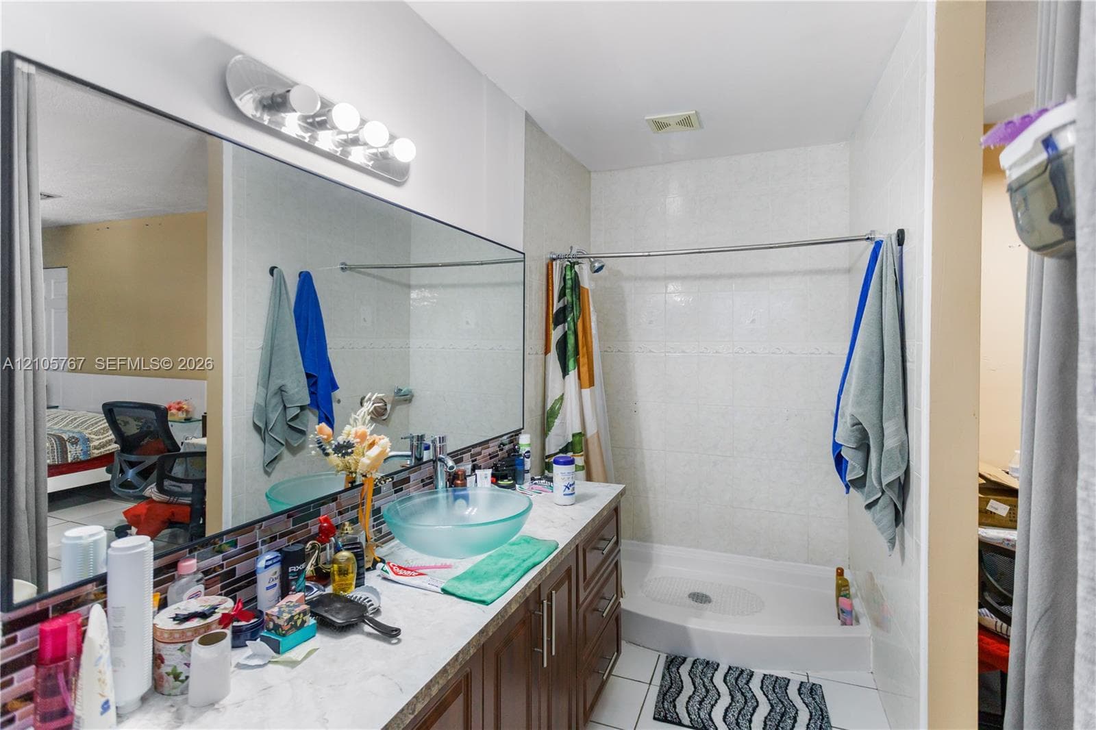 Full-width mirror, wood-finish vanity cabinetry, glass vessel sink, mosaic tile backsplash, and stand-alone shower with tiled walls
