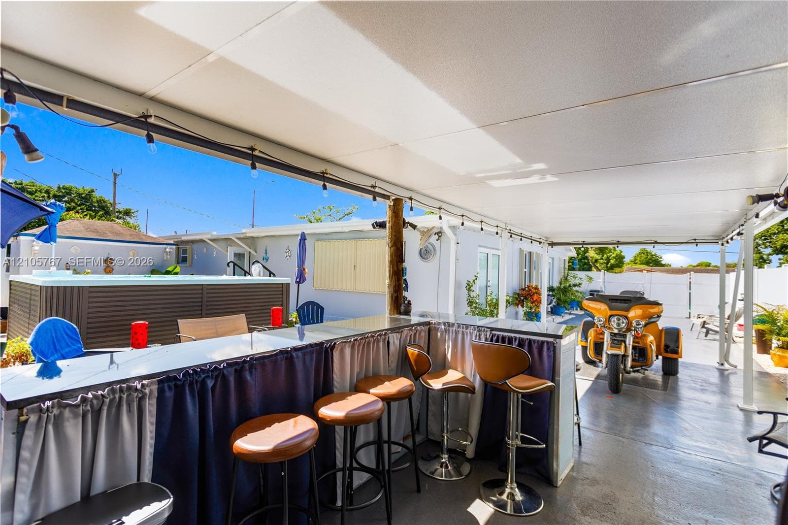 Covered outdoor patio area featuring a built-in wet bar with a countertop, an overhead string lighting system, and a built-in spa
