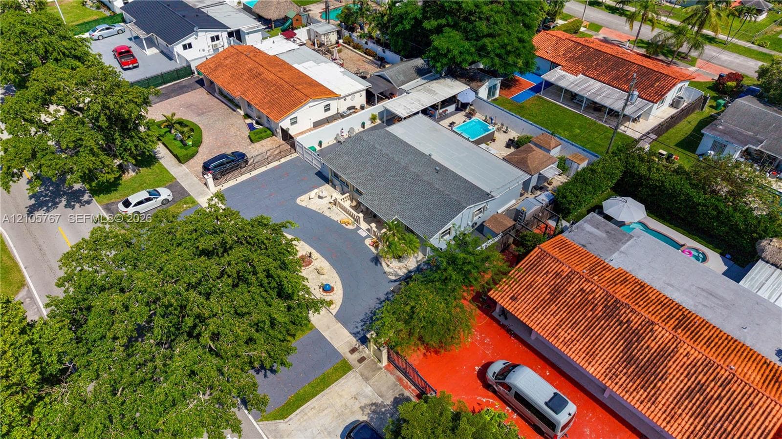 Aerial perspective featuring a paved driveway, asphalt shingle roofing, and established mature trees