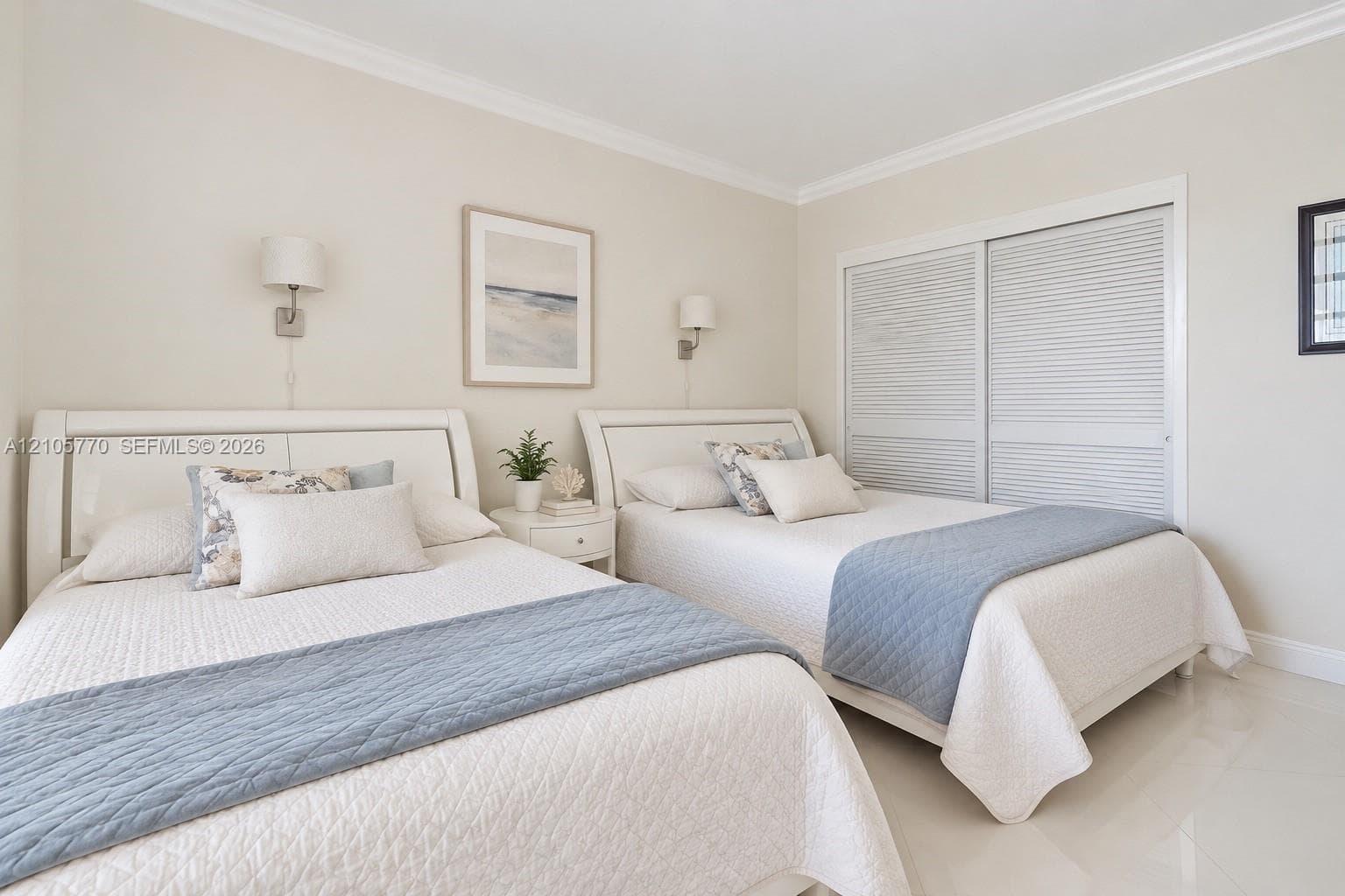 Neutral-toned interior featuring crown molding, polished tile flooring, wall-mounted light fixtures, and white louvered-style sliding closet doors