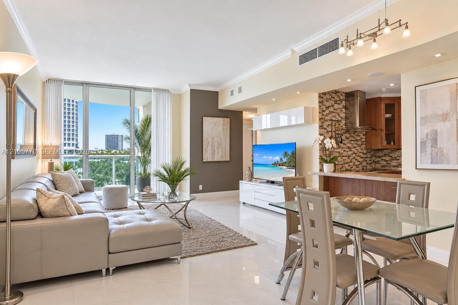 Contemporary open-concept living space featuring floor-to-ceiling windows with city skyline backdrop, light wood-finish flooring throughout, neutral upholstered seating, glass-top dining table with metal base, stone accent wall with integrated media niche, recessed and pendant lighting, and modern kitchen cabinetry with white finishes