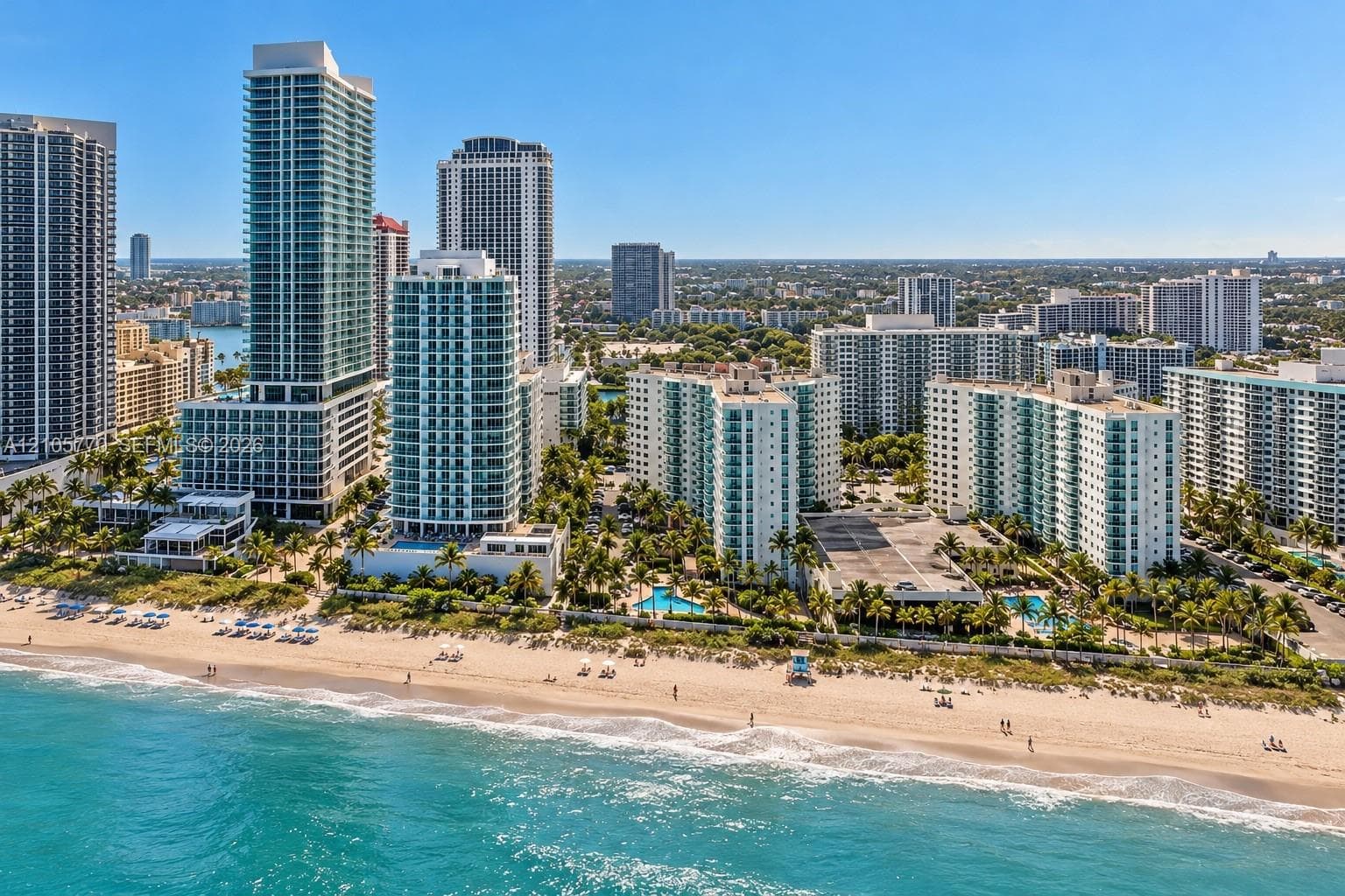 Coastal high-rise residential complex featuring private beach access, exterior balconies, swimming pools, and extensive palm tree landscaping