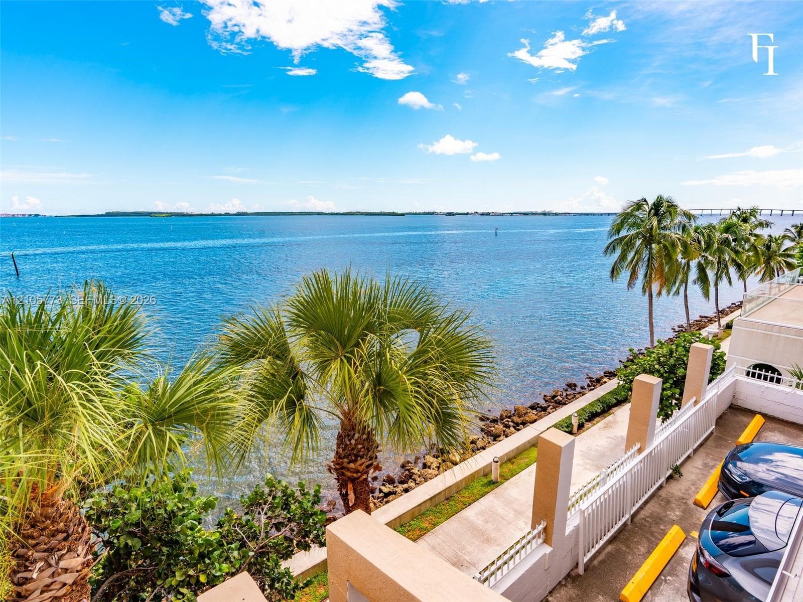 Waterfront property featuring unobstructed coastal scenery, mature palm trees, a concrete bulkhead, and a paved walkway along the shoreline