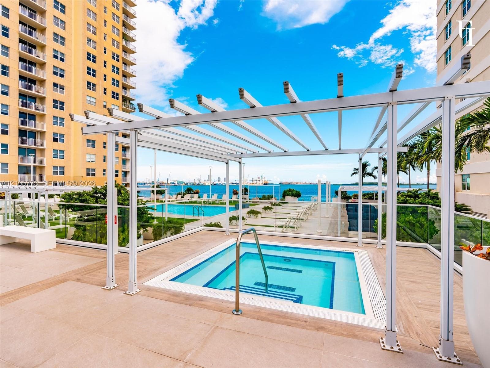 Outdoor spa featuring a metal pergola, composite decking, and glass railings overlooking the water