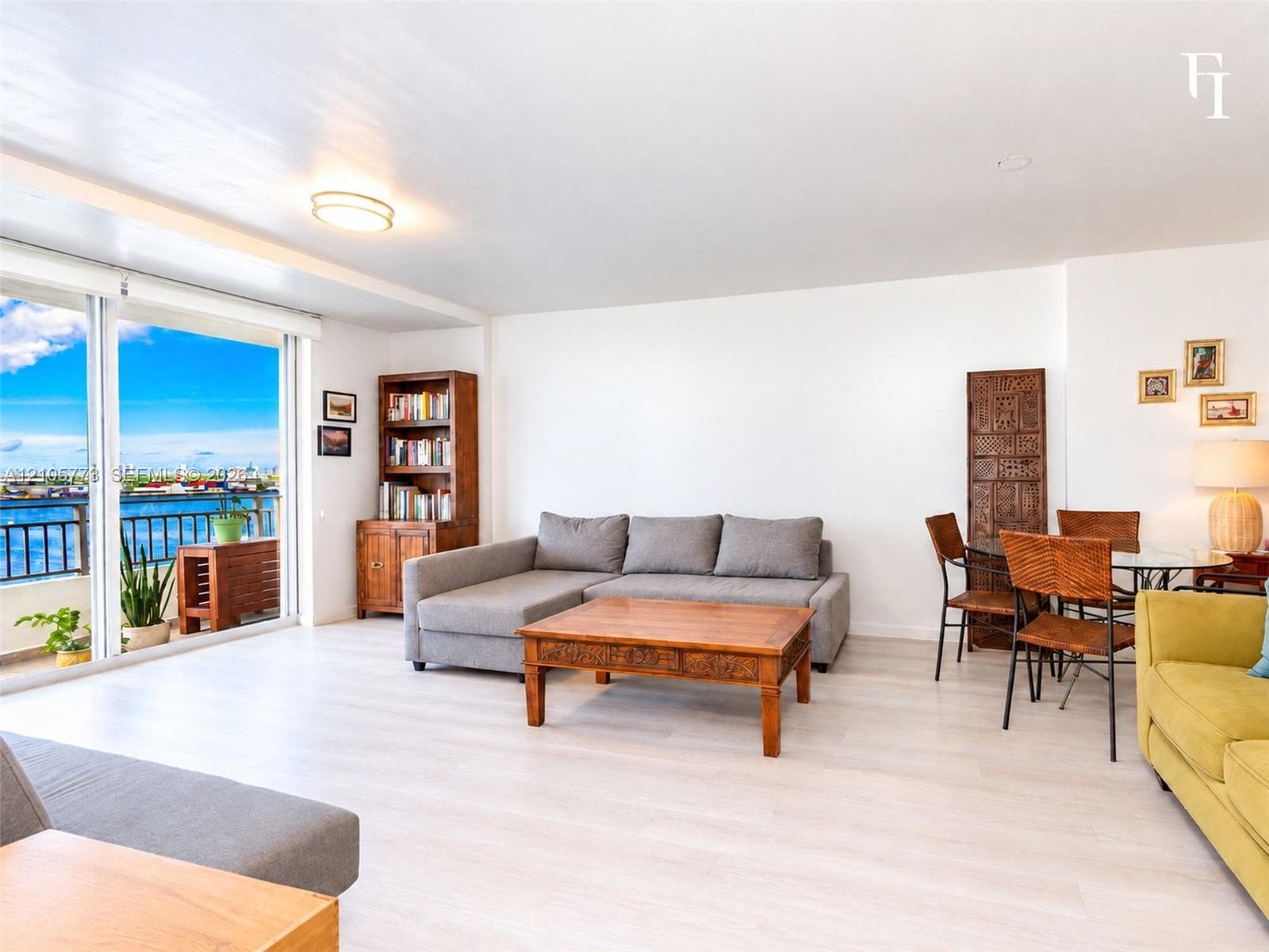 Open-concept living space featuring wood-finish flooring, sliding glass doors, and a metal-railed balcony with water scenery