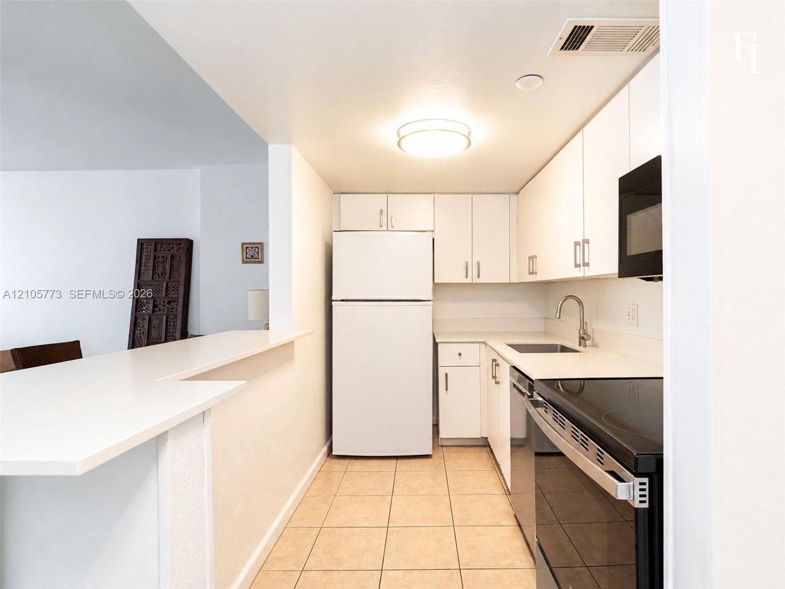 Kitchen featuring white cabinetry, solid-surface countertops, tile flooring, and integrated black appliances