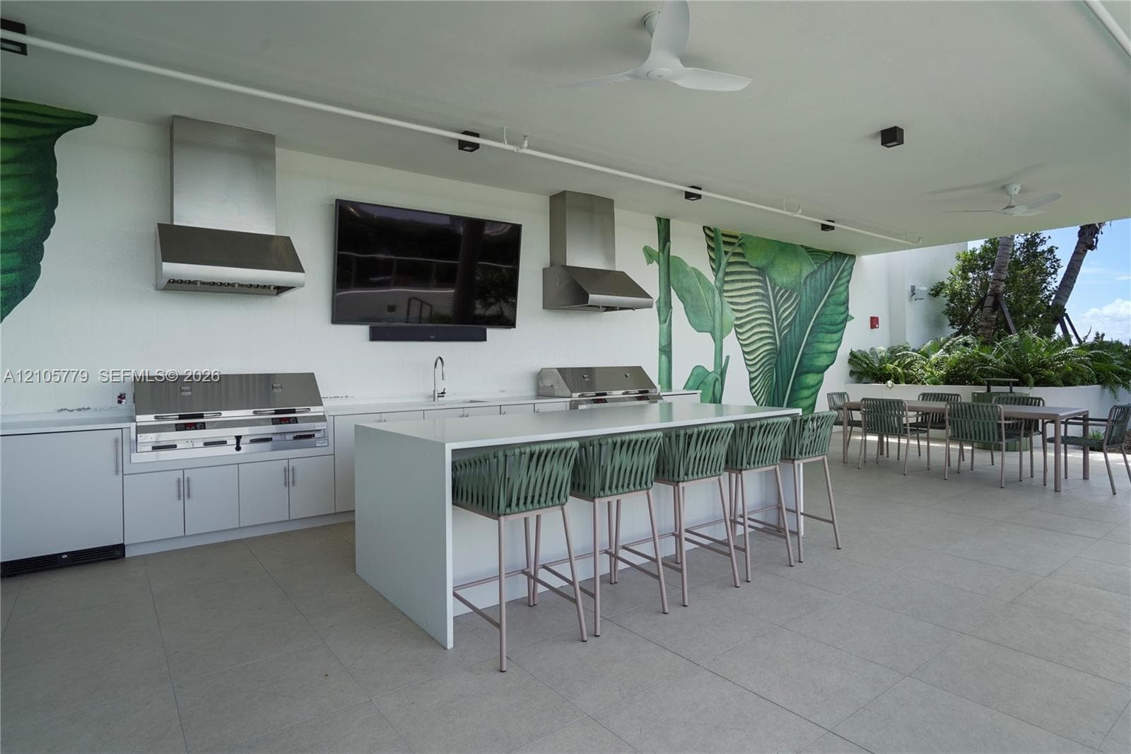 Covered outdoor kitchen featuring a stone-topped island, stainless steel built-in grills, dual stainless steel range hoods, and tile flooring