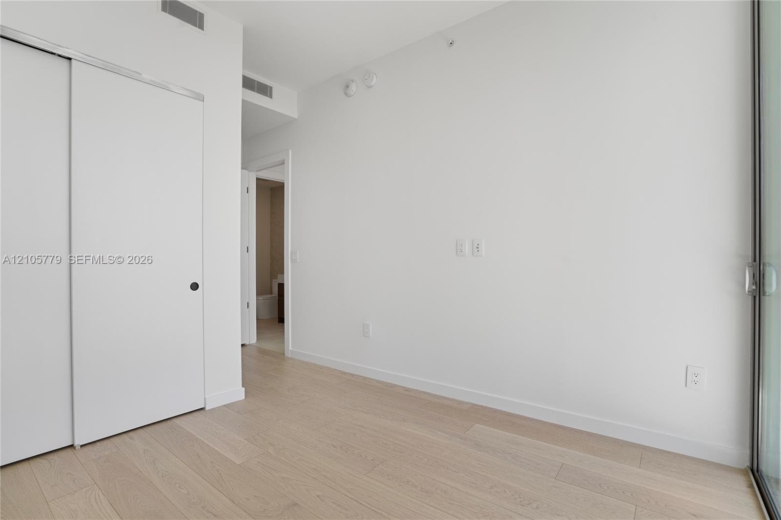 Interior space featuring light wood-finish flooring, sliding door closet, floor-to-ceiling glass paneling, and smooth-finish white walls