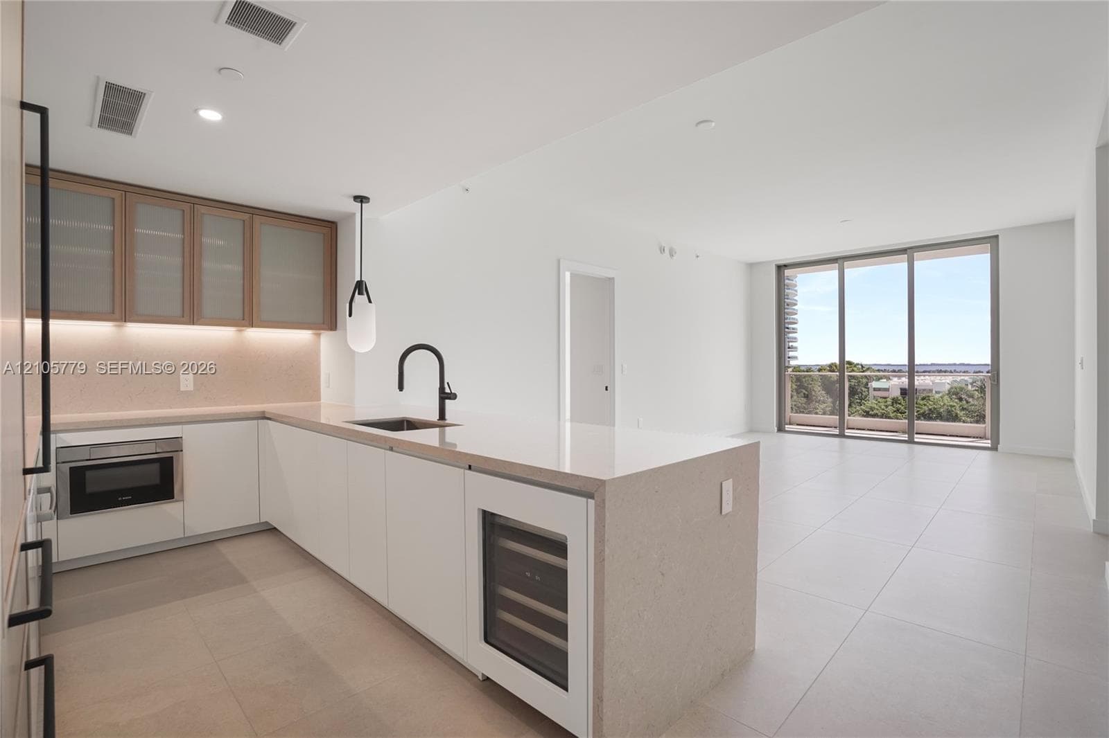 Modern kitchen featuring white flat-panel cabinetry, light-toned stone countertops, a waterfall-edge island, built-in wine refrigeration, and a matte black faucet