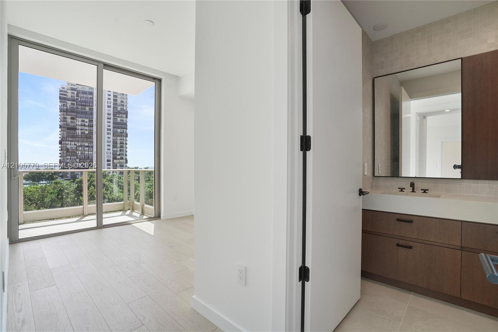 Floor-to-ceiling sliding glass door, private balcony, wood-finish flooring, floating vanity with dual-toned cabinetry, and large rectangular wall mirror