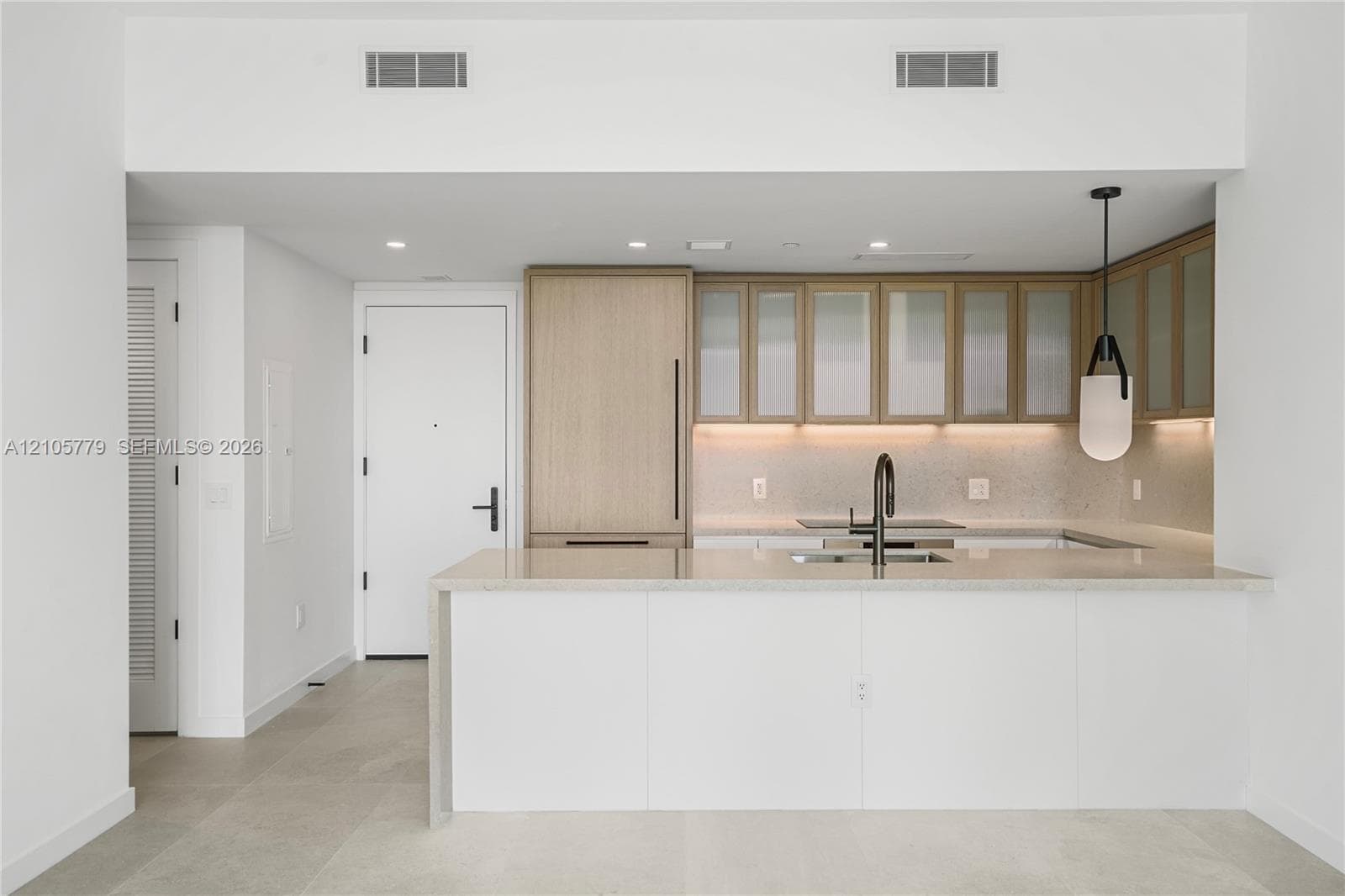 Kitchen featuring light wood-finish cabinetry with frosted glass inserts, a white quartz waterfall-edge island, integrated refrigerator, matte black gooseneck faucet, and under-cabinet lighting
