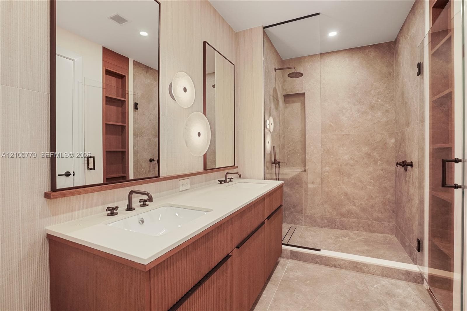 Double vanity with a composite countertop, fluted wood-finish cabinetry, walk-in shower with stone-tile surround, glass enclosure, and wall-mounted plumbing fixtures
