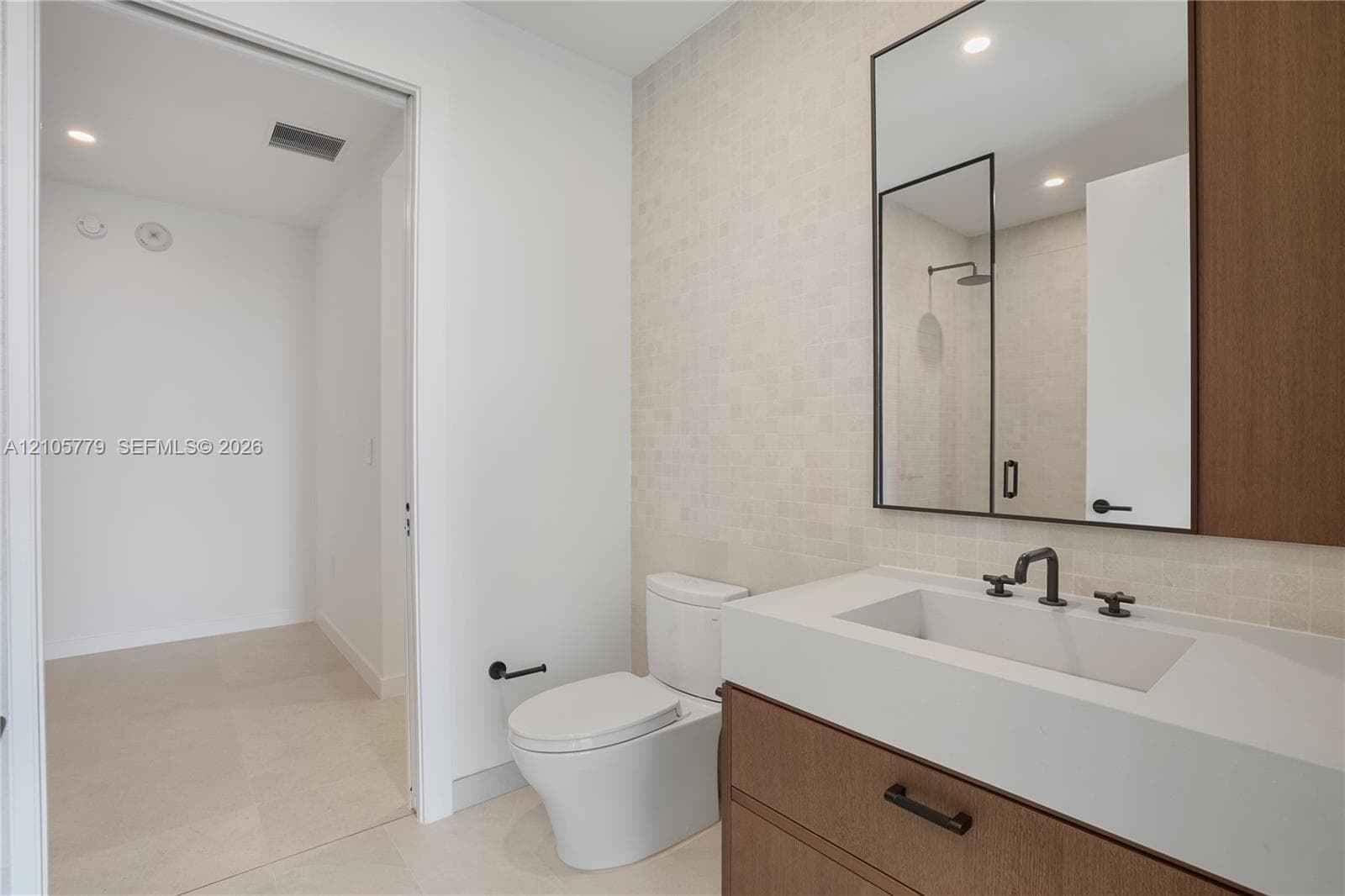 Floating wood-finish vanity with a stone countertop, rectangular undermount sink, matte black widespread faucet, and matching framed mirror, complemented by tile wall detailing and recessed lighting