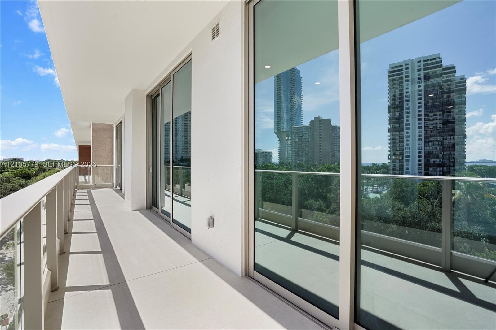 Expansive covered balcony featuring glass panel railings, floor-to-ceiling sliding glass doors, and neutral concrete-style flooring