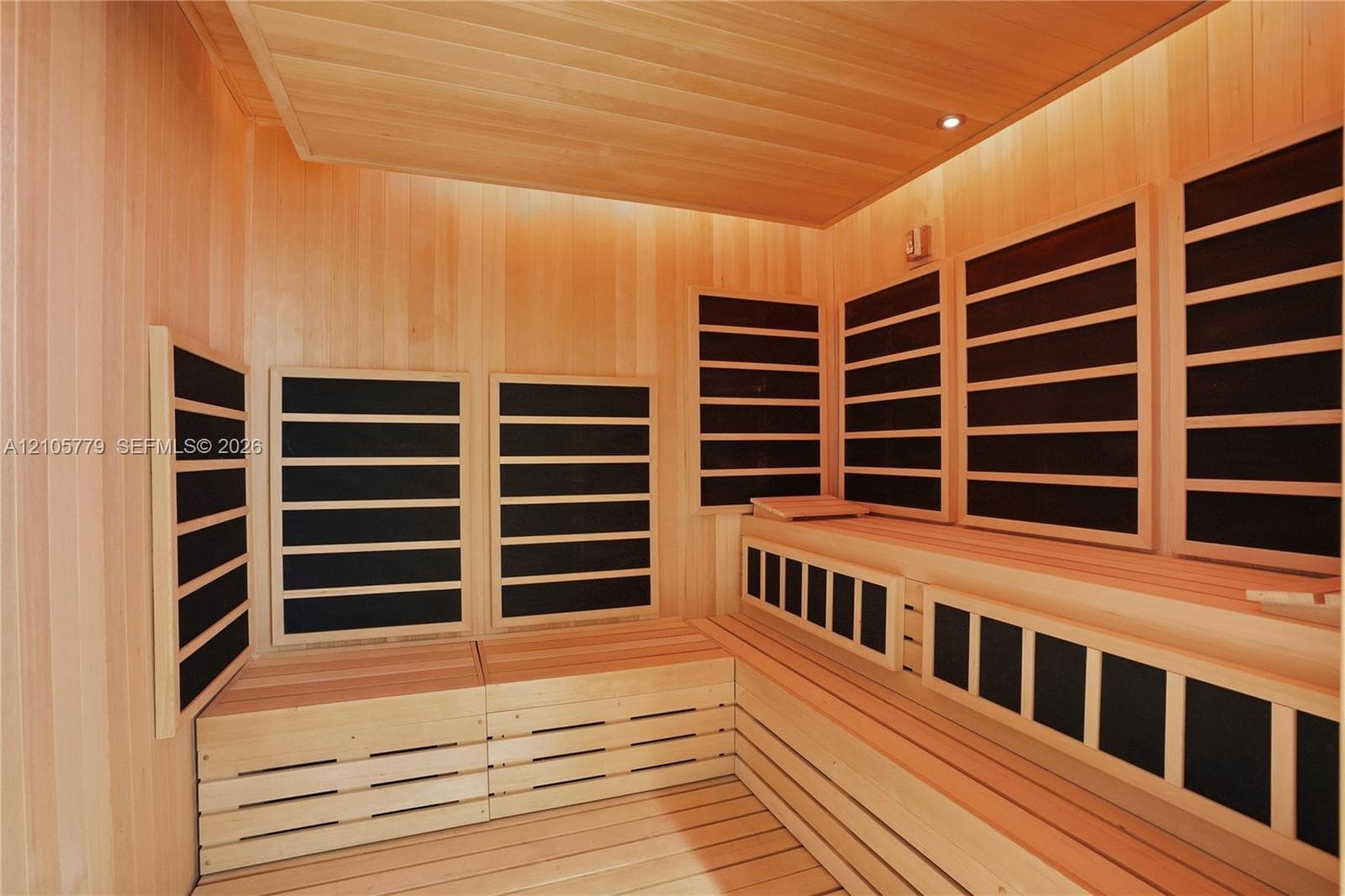 Sauna room featuring light wood-panelled walls, built-in tiered bench seating, infrared heating panels, and recessed ceiling lighting