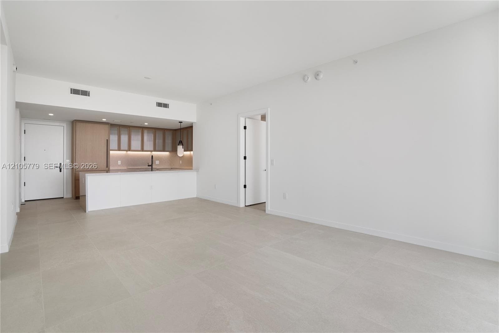 Open-concept interior with large-format neutral tile flooring, minimalist kitchen featuring light wood-tone cabinetry, stone-surface breakfast bar, and integrated cabinetry