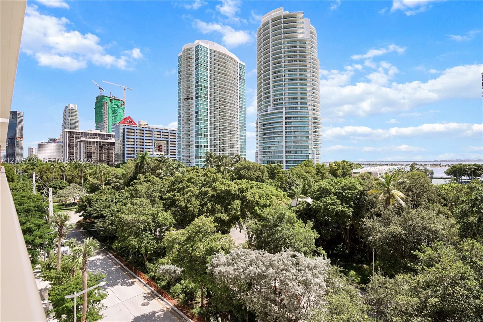 Exterior balcony featuring a concrete railing, mature tree canopy, and skyline backdrop