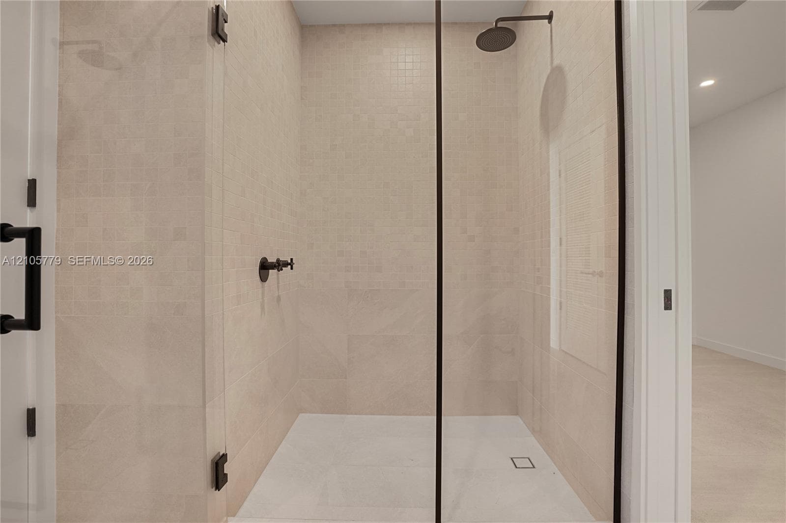Walk-in shower featuring floor-to-ceiling neutral tile, glass enclosure with matte black hardware, rainfall showerhead, and wall-mounted matte black faucet