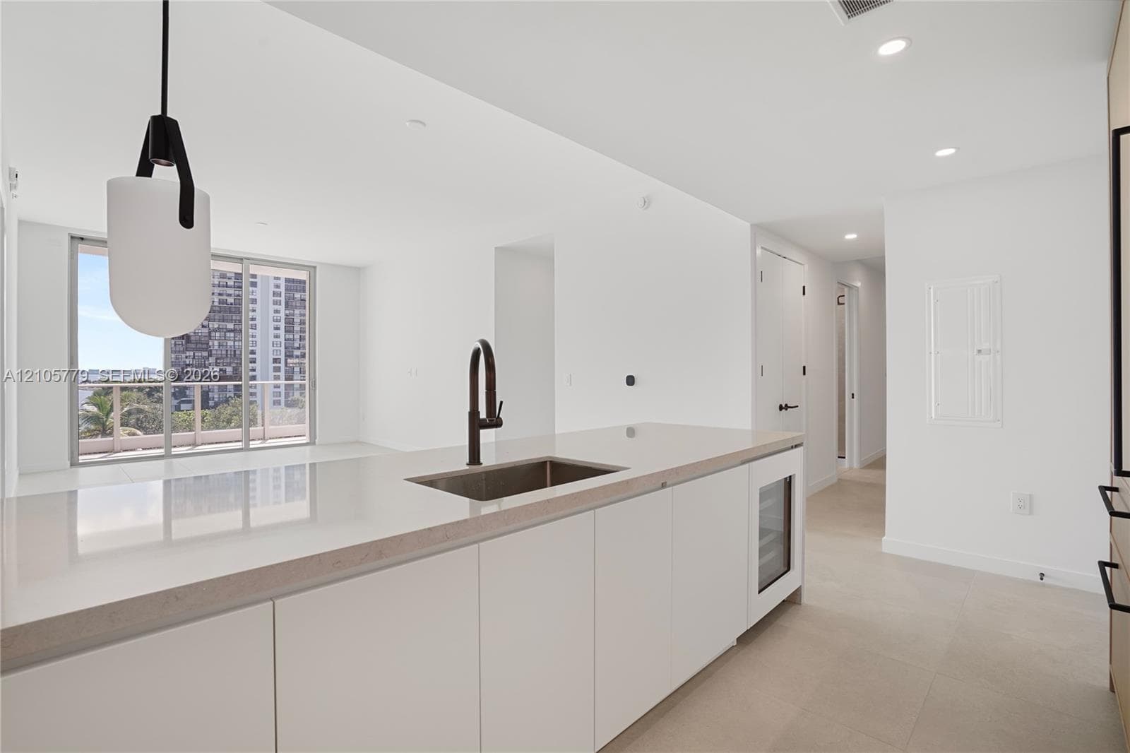 Kitchen island featuring a stone countertop, undermount sink with a matte black faucet, built-in under-counter beverage chiller, and modern pendant lighting