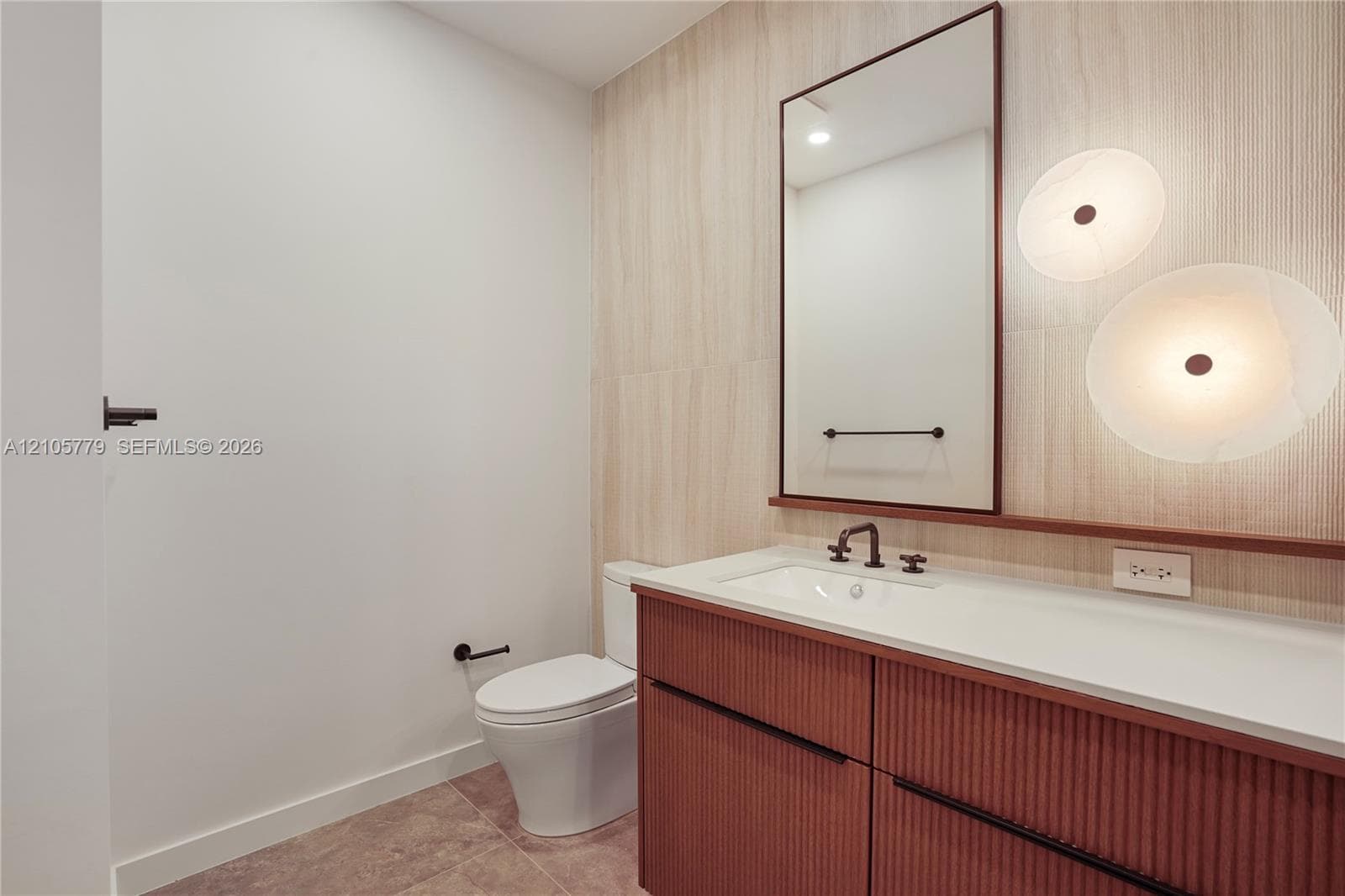 Powder room featuring a fluted wood vanity, integrated white countertop, wall-mounted matte black faucet, vertical textured wall tiling, and dual circular wall sconces