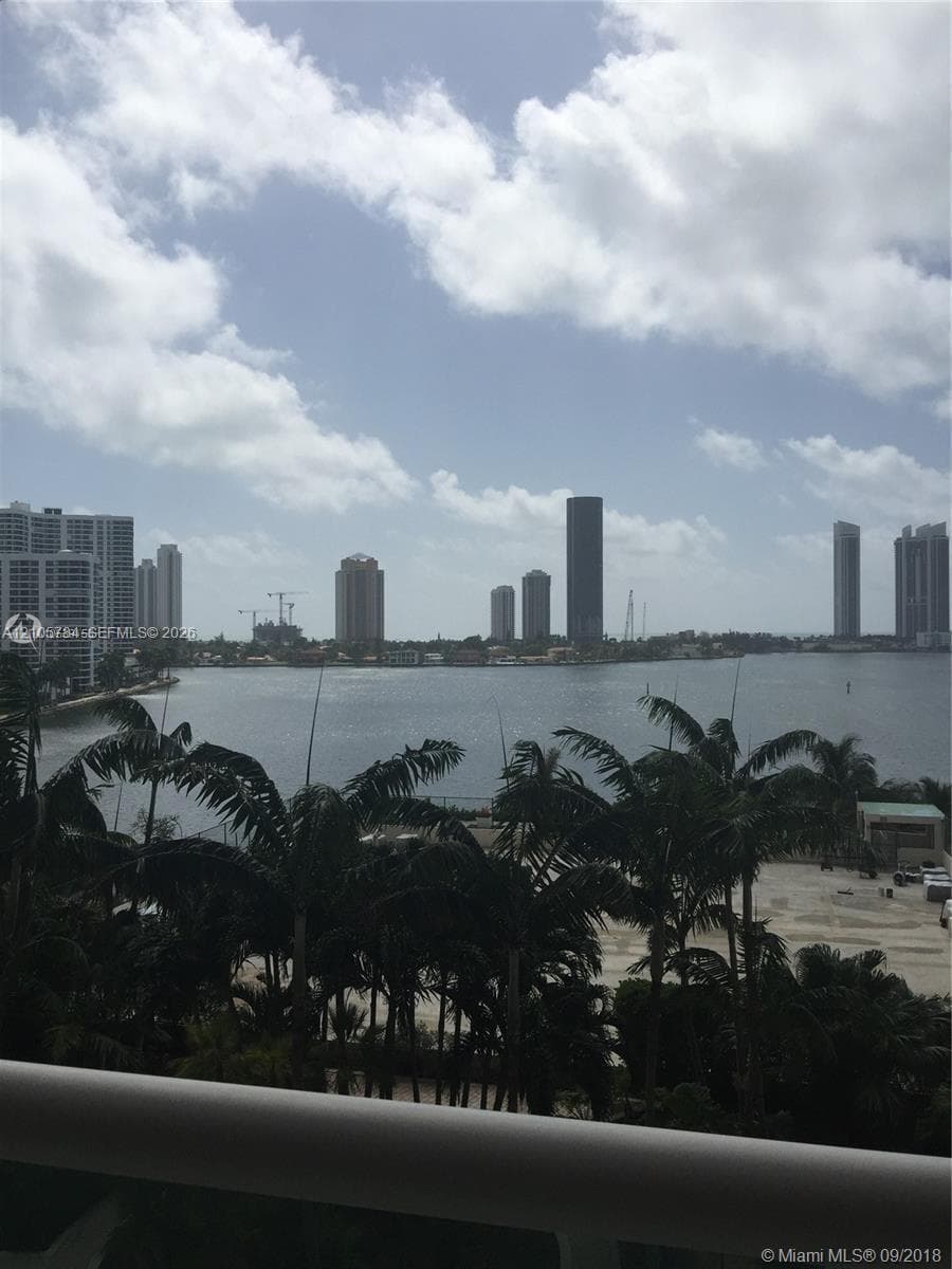 Waterfront balcony featuring a metal railing, palm trees, and panoramic cityscape