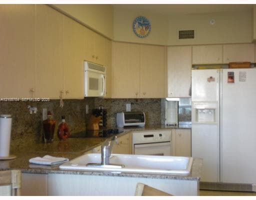 Kitchen featuring light-finish cabinetry, stone countertops, stone backsplash, white undermount sink with a chrome faucet, and built-in appliances