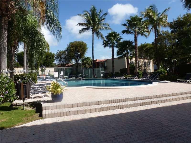 In-ground swimming pool featuring concrete paver decking, multi-level stairs, perimeter fencing, and surrounding palm trees