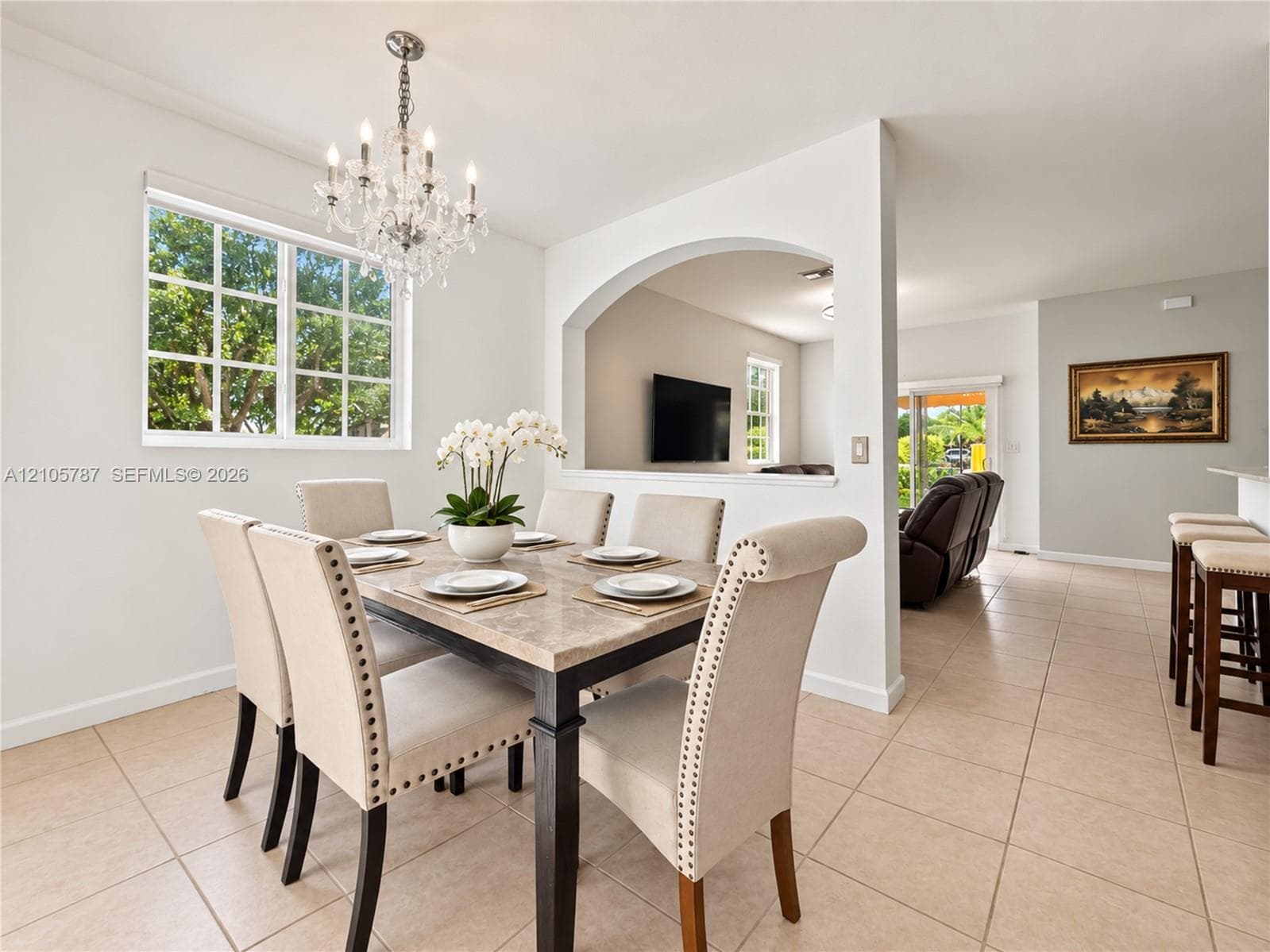 Dining area featuring a multi-pane window, crystal chandelier, arched architectural opening, and ceramic tile flooring