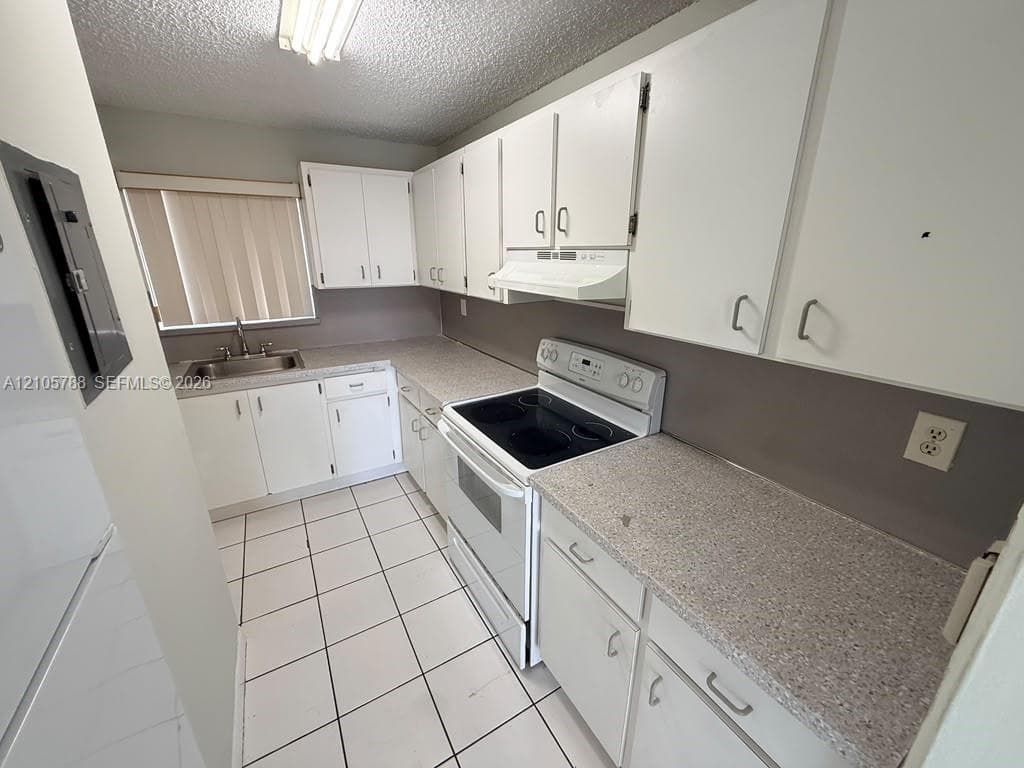 Kitchen featuring white cabinetry, solid-surface countertops, tile flooring, integrated range hood, and double-basin stainless steel sink