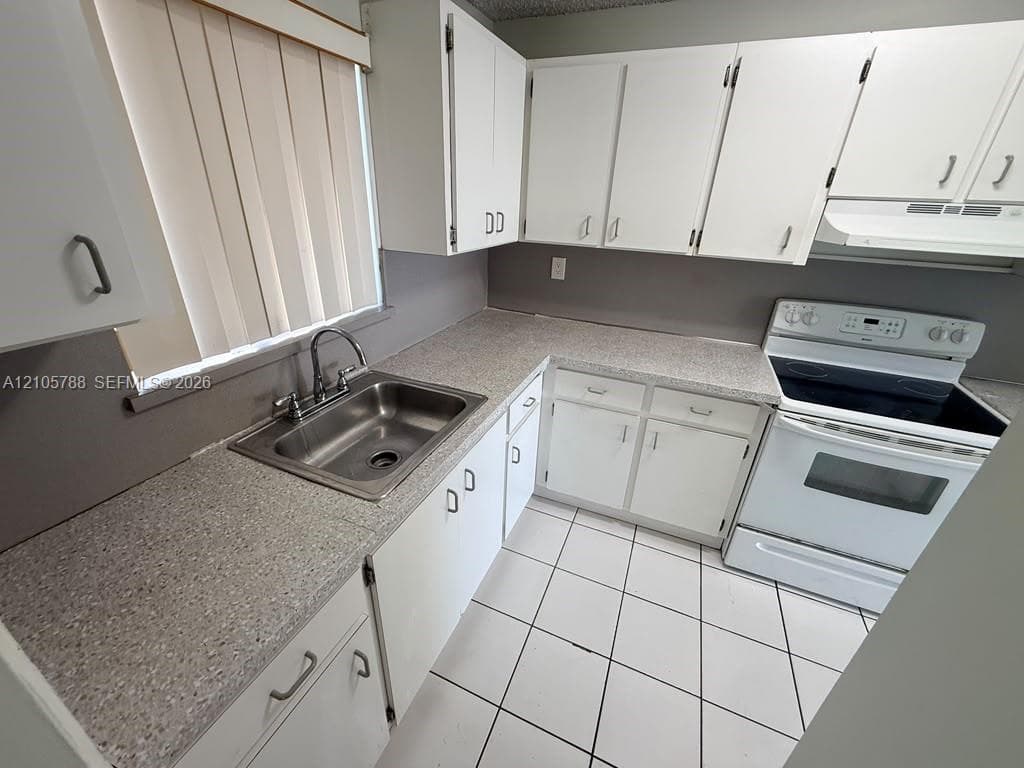 Kitchen featuring white cabinetry, speckled laminate countertops, a stainless steel dual-basin sink, an integrated range, and tiled flooring