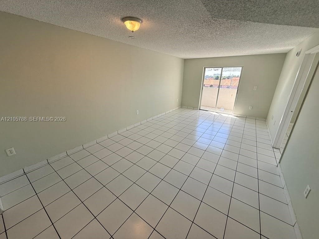 Spacious room featuring white tile flooring, neutral wall tones, a ceiling-mounted light fixture, and glass sliding doors