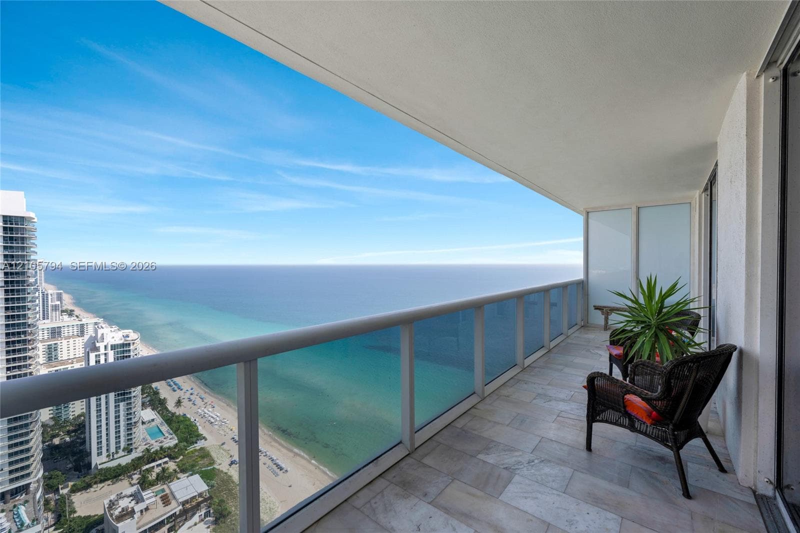 Covered balcony featuring stone tile flooring and a glass panel railing