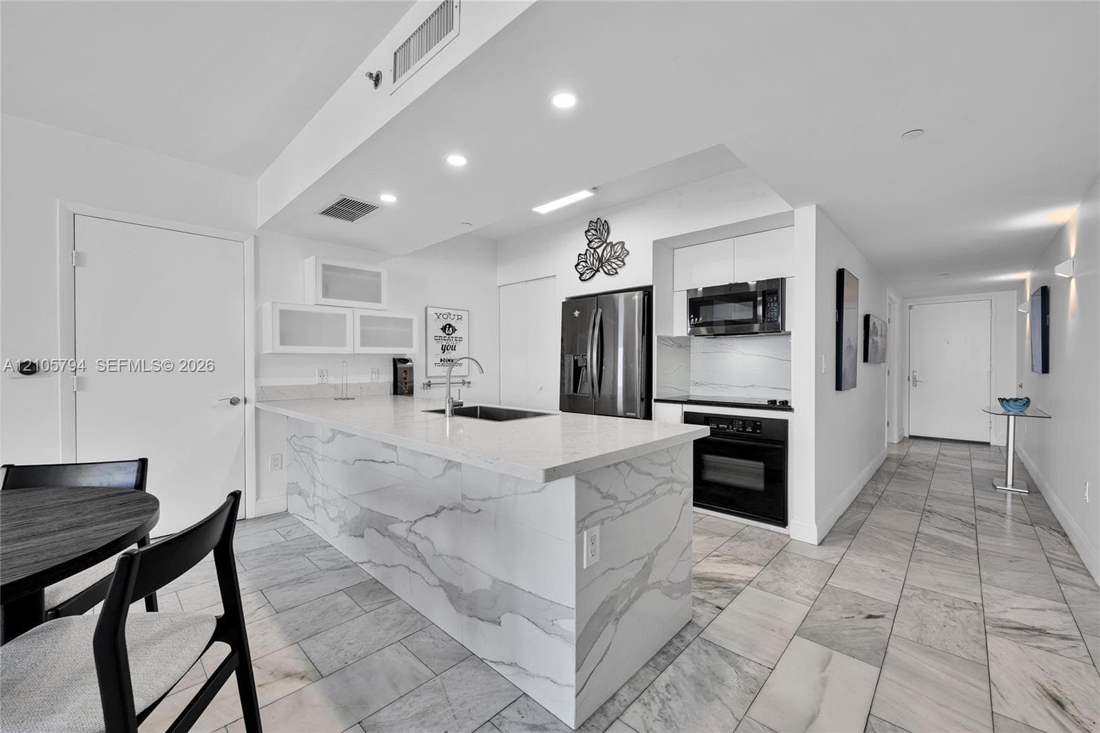 Kitchen featuring a quartz waterfall island, stone-finish tile flooring, white cabinetry, stainless steel appliances, and recessed lighting