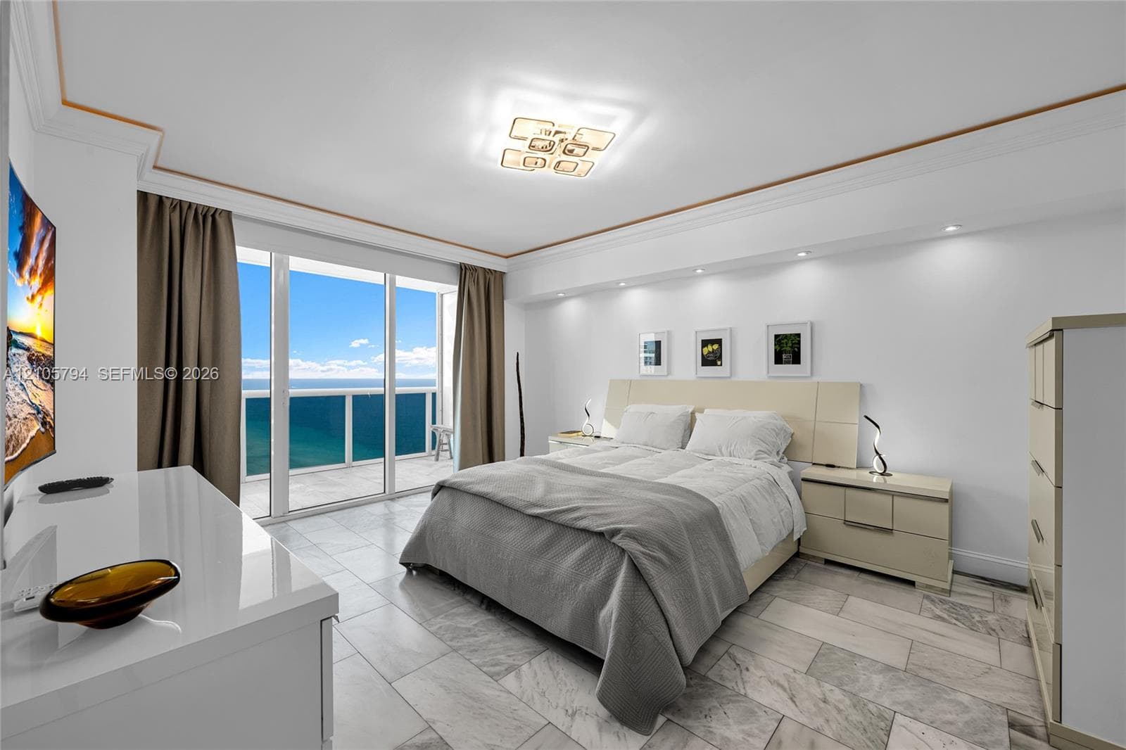 Stone flooring, recessed ceiling lighting, decorative crown molding, and floor-to-ceiling glass doors opening to a balcony with ocean exposure