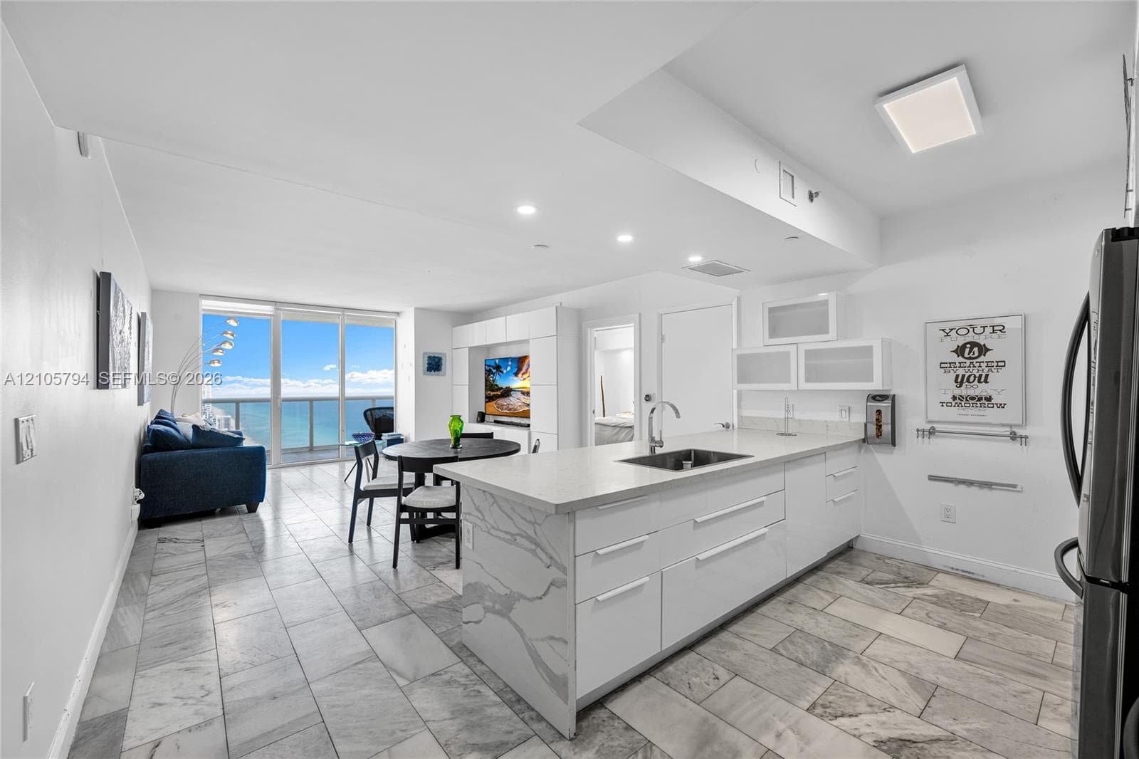 Open-concept interior featuring stone flooring, kitchen island with stone waterfall countertop, built-in cabinetry, recessed lighting, and floor-to-ceiling glass panel windows