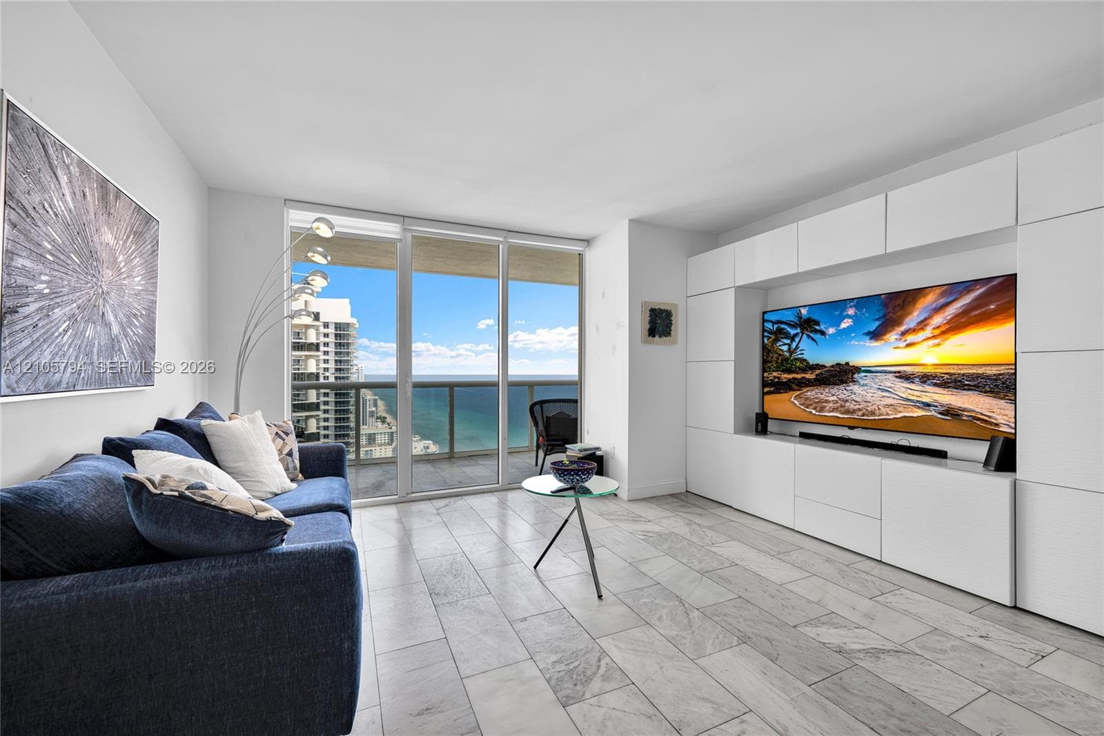 Living area featuring large-format tile flooring, floor-to-ceiling glass doors, and a custom built-in white cabinetry wall unit